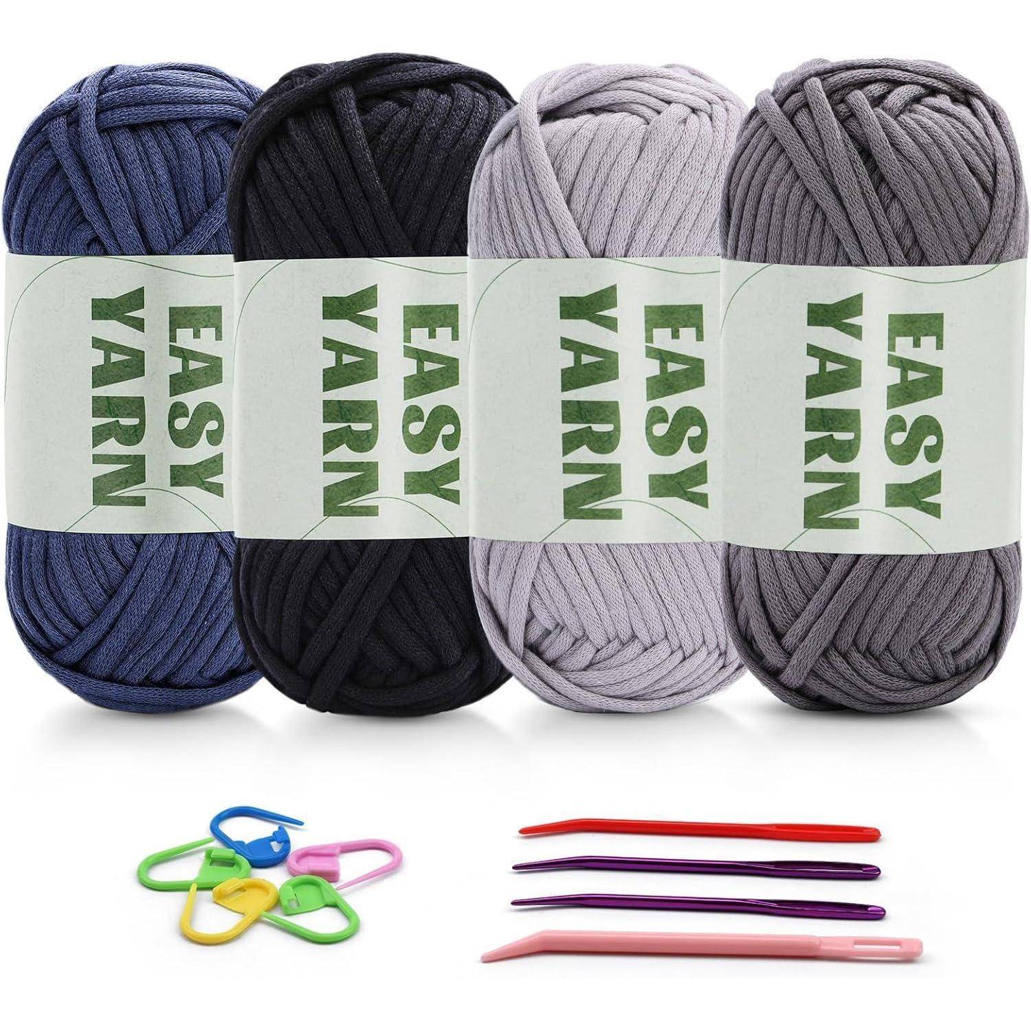 Vier Knäuel 'Easy Yarn' in Blau, Schwarz, Hellgrau und Grau werden zusammen mit bunten Maschenmarkierern und Häkelnadeln präsentiert.
