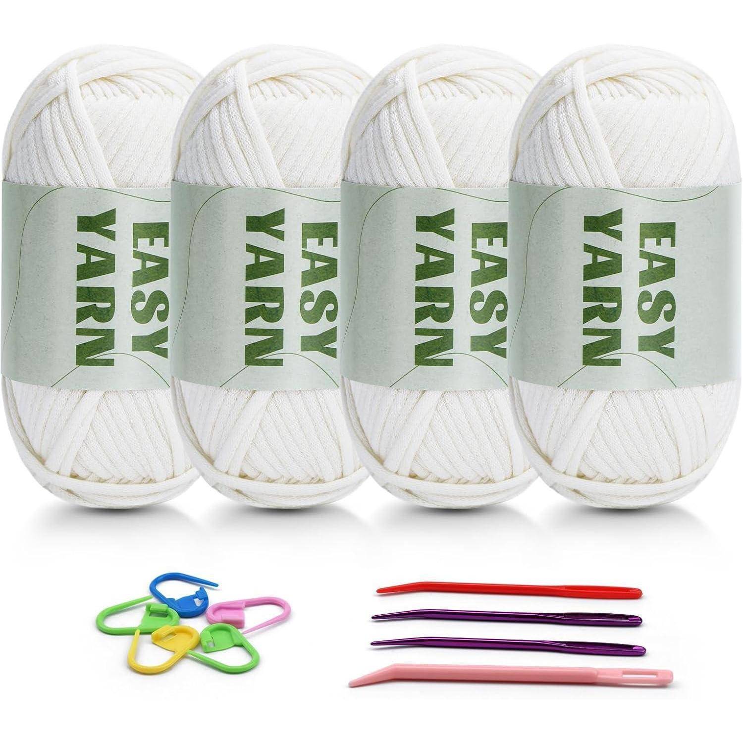 Vier Knäuel weißes ‚Easy Yarn', bunte Maschenmarkierer und Häkelnadeln in verschiedenen Farben, ordentlich darunter angeordnet.