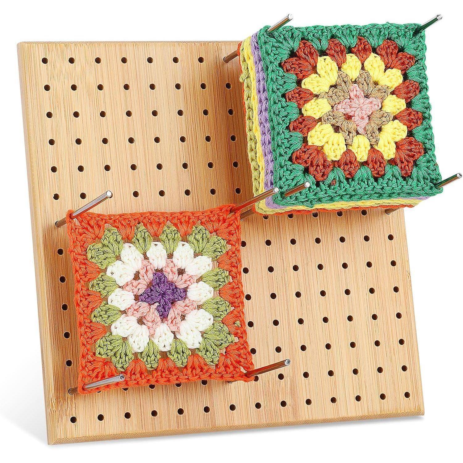 Zwei bunte gehäkelte Granny-Squares, eines in Erdtönen und eines in leuchtenden Farben, sind an einer Holzlochplatte mit Metallstäben befestigt.