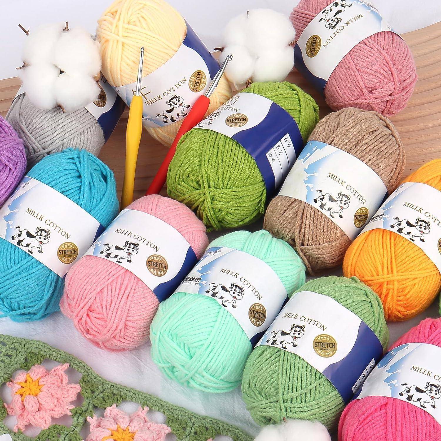 Verschiedene farbenfrohe Wollbälle, darunter rosa, blau, grün, beige und gelb, sind zusammen mit Häkelnadeln und Baumwollblumen angeordnet.