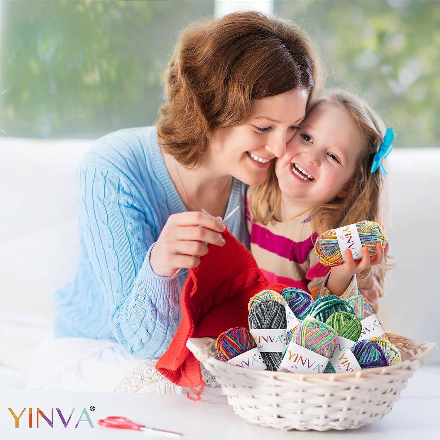 Eine Mutter und ihre Tochter lächeln, während sie bunte Wollbälle halten und auf einem Sofa sitzen. Ein Korb mit Wollbällen steht auf dem Tisch vor ihnen.