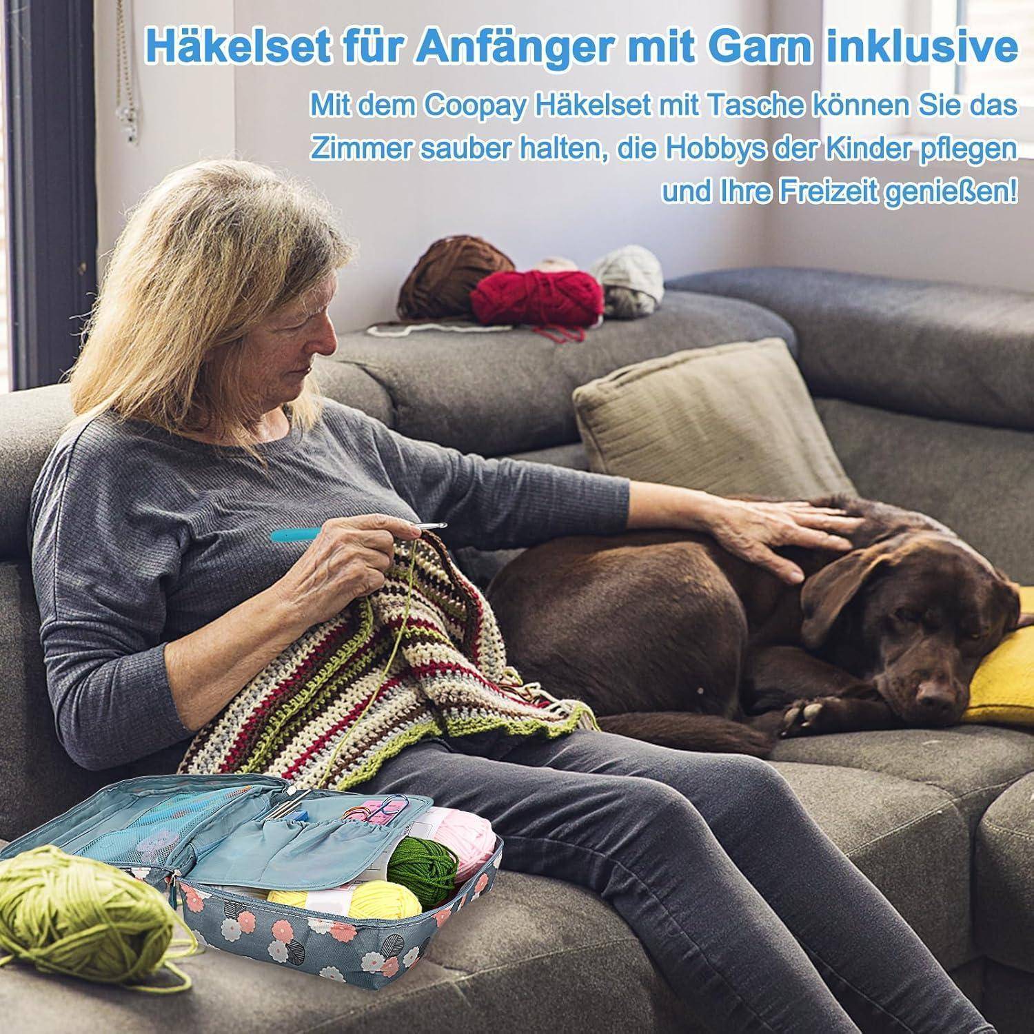 Eine Frau sitzt auf einem Sofa und häkelt, während ein Hund neben ihr ruht. Ein Häkelset mit Garn liegt auf dem Tisch. Text auf Deutsch oben.