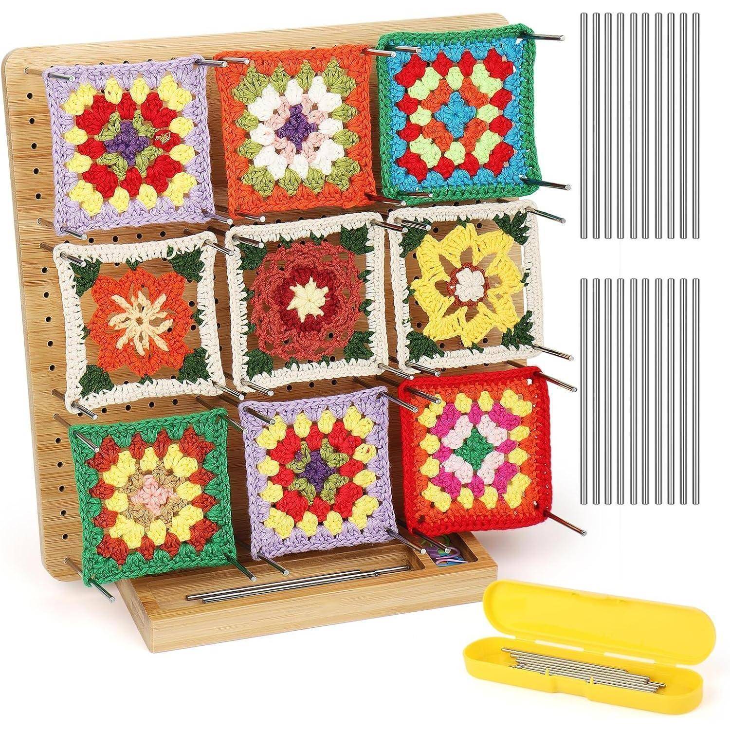 Ein Holzblock hält neun bunte gestrickte Quadrate, die jeweils mit dünnen Stecknadeln befestigt sind. Ein gelber Werkzeugkasten steht neben dem Block.