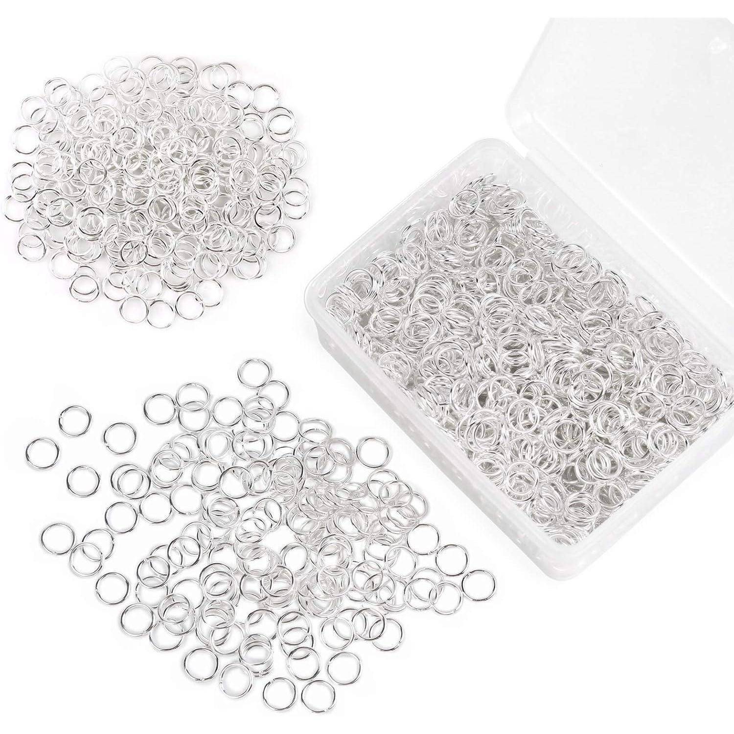 Ein Plastikbehälter mit vielen kleinen, silbernen Sprungringen, von denen einige nach außen verschüttet sind. Verwendet für Schmuckherstellung oder Handarbeiten.