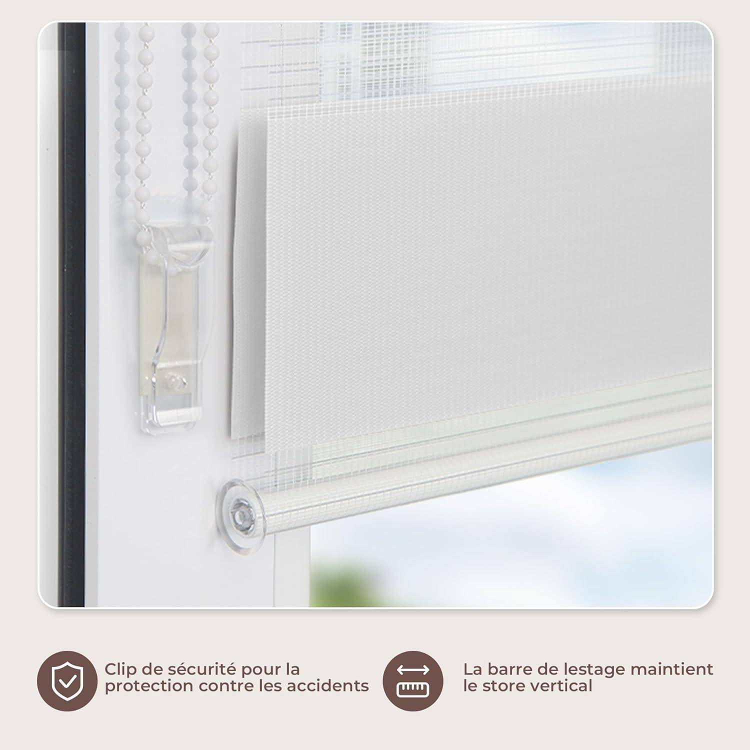 Eine Nahaufnahme eines Fensters mit einer weiß-en Rolljalousie, die teilweise heruntergelassen ist, mit einem Sicherheitsclip und einer Steuerkette auf der linken Seite.