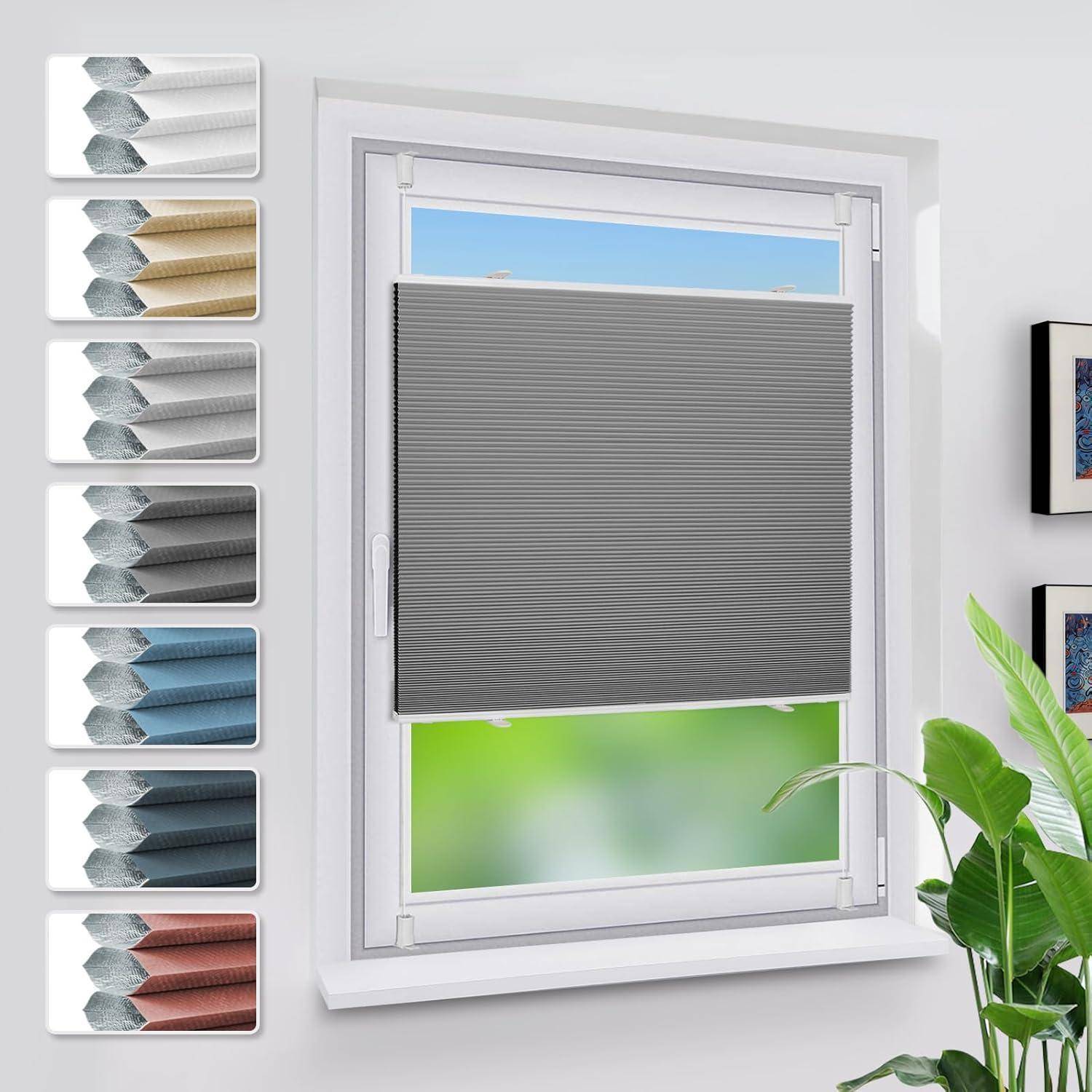 Ein Fenster mit einer halb geöffneten, grauen Plisseejalousie ist zu sehen. Auf der linken Seite sind Stoffmuster in verschiedenen Farben ausgestellt.