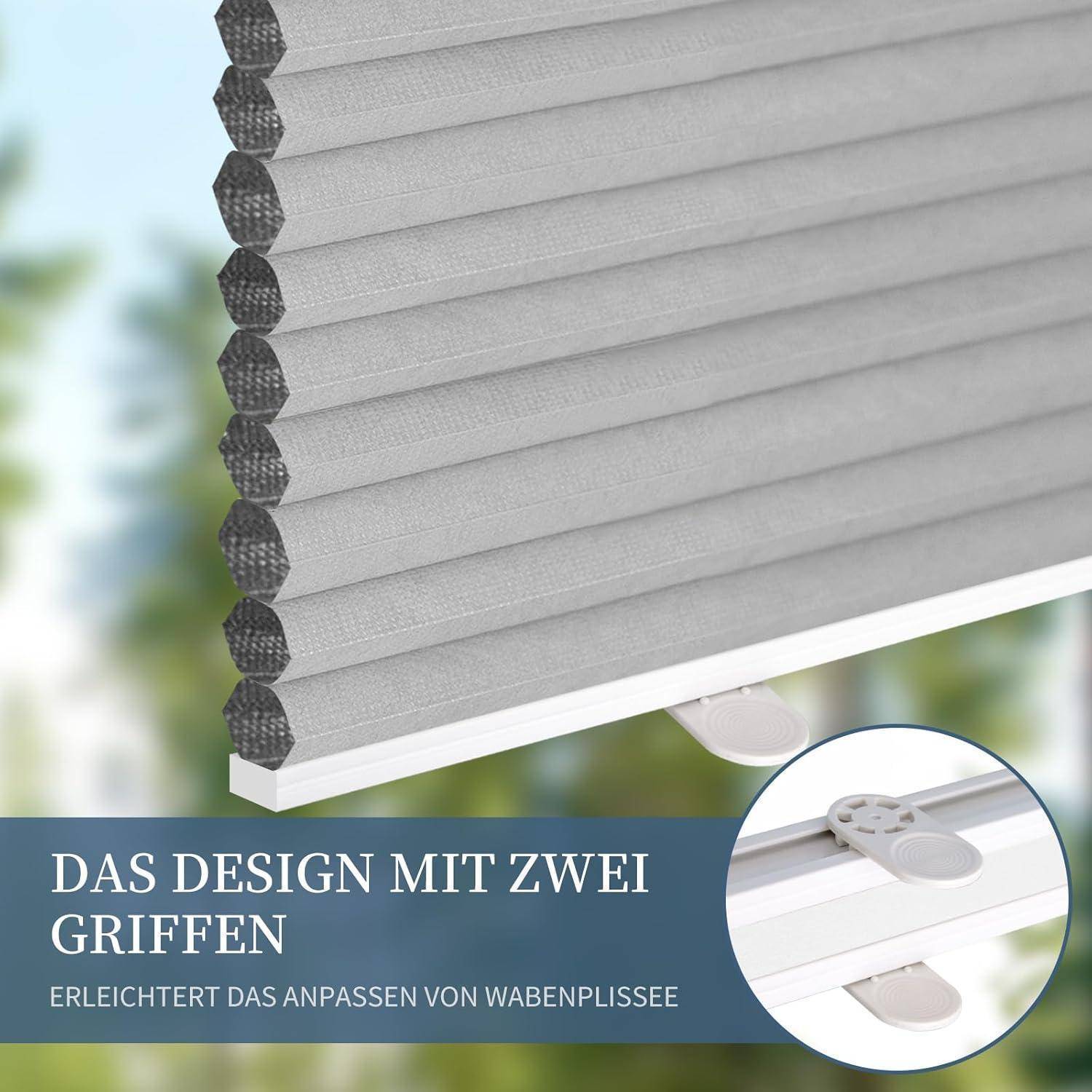 Eine Nahaufnahme eines Wabenrollos mit zwei Griffen, mit der Beschriftung 'Das Design mit zwei Griffen'. Im Hintergrund sind verschwommene Grünpflanzen zu sehen.