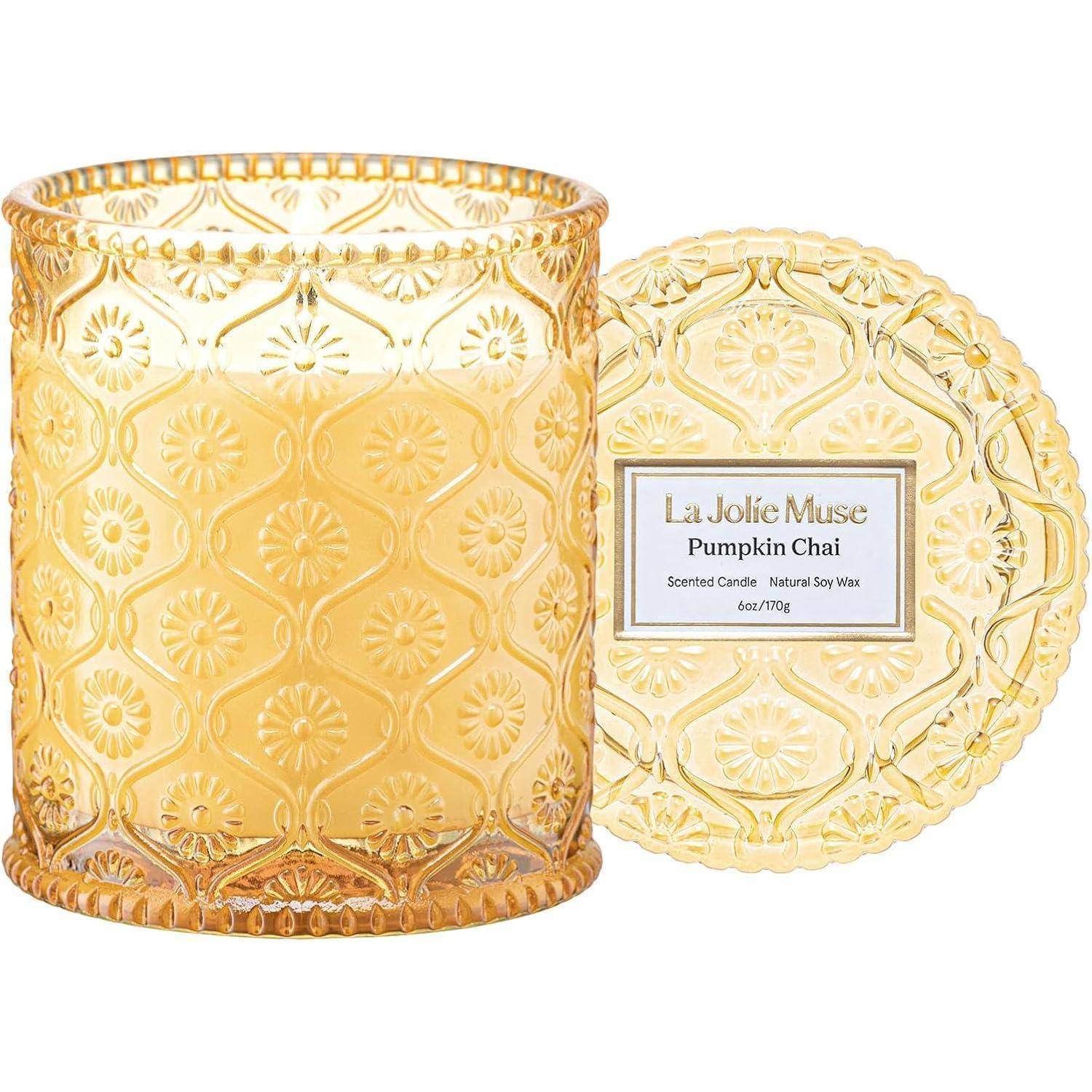 Ein gemustertes Glasgefäß enthält eine Duftkerze von 'La Jolie Muse' mit dem Duft Kürbis Chai und einem passenden Deckel, was eine gemütliche, aromatische Atmosphäre andeutet.