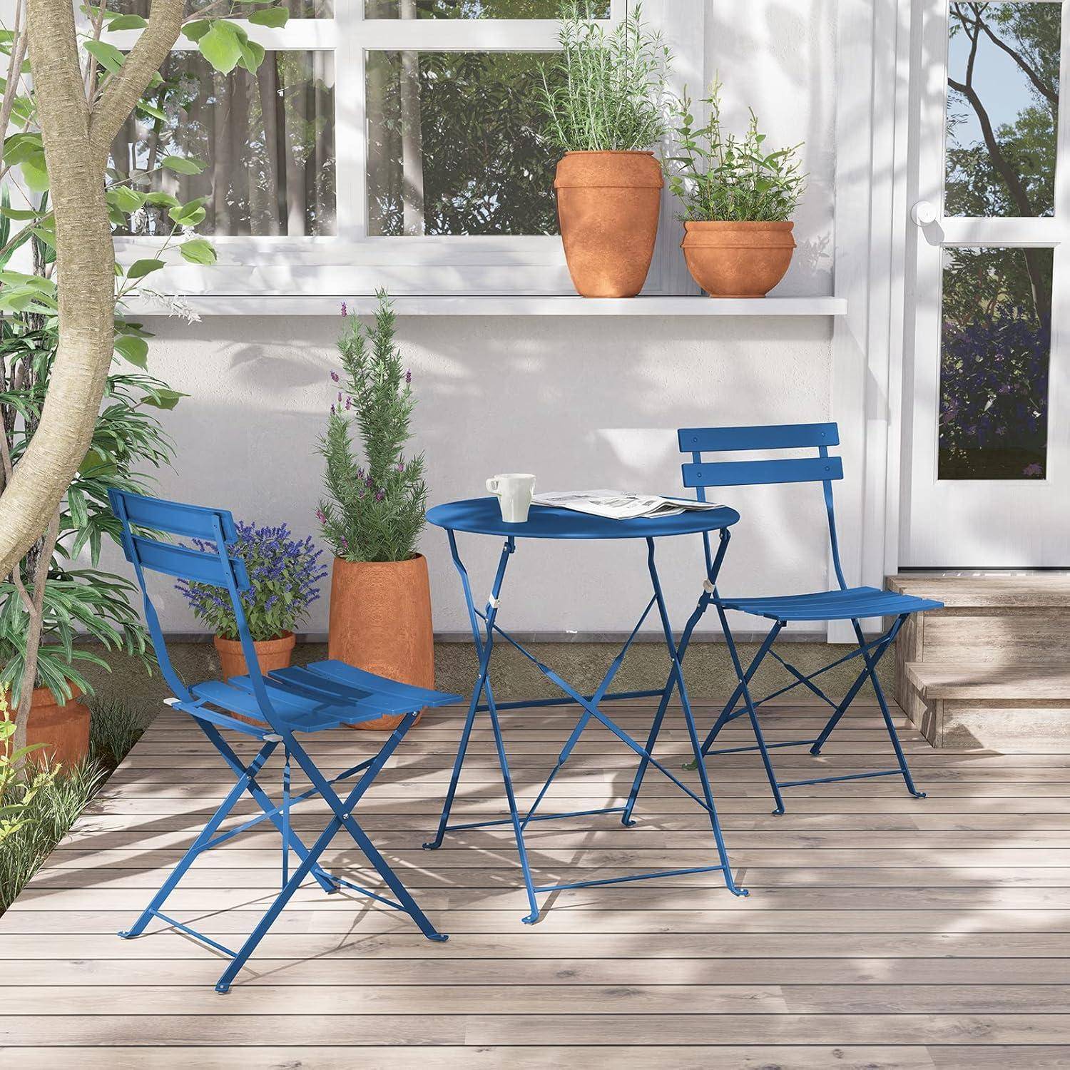 Eine sonnige Terrasse mit zwei blauen Metallstühlen und einem passenden Tisch. Topfpflanzen schmücken die Fläche, während Sonnenlicht durch die Blätter filtert.