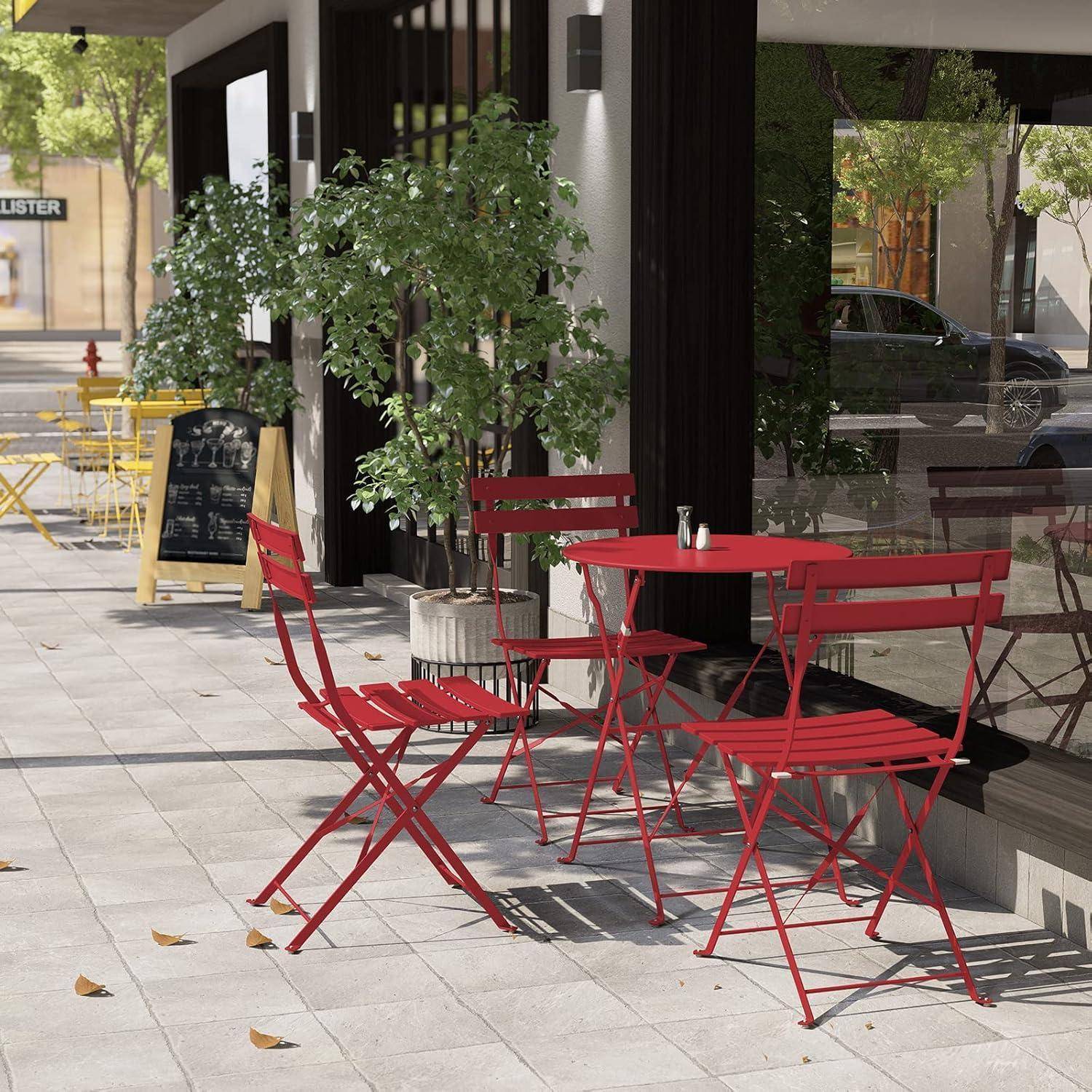 Straßencafé mit roten Metalltischen und -stühlen, umgeben von grünen Pflanzen. Eine Kreidetafel-Speisekarte ist in der Nähe des Eingangs sichtbar. Bäume säumen die Straße.