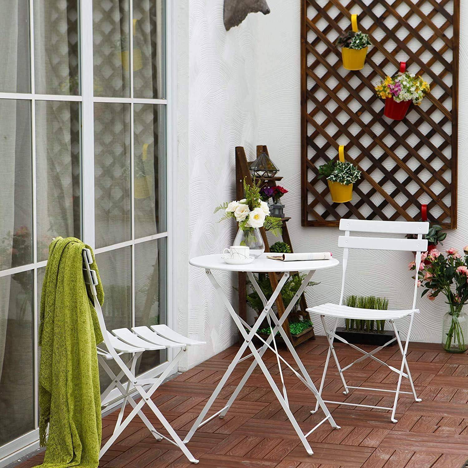 Eine gemütliche Terrasse mit einem kleinen runden Tisch und zwei Stühlen. Blumen in Töpfen hängen an einem Spalier, und eine grüne Decke liegt über einem Stuhl.