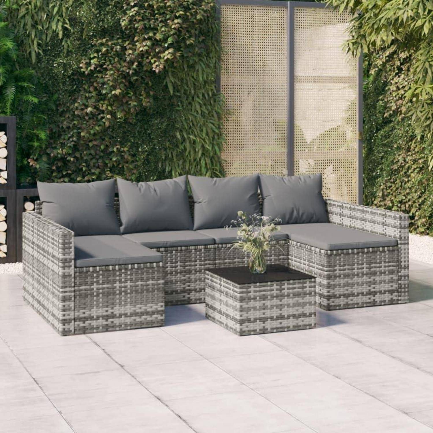 Outdoor-Terrassenmöbel mit Möbeln aus grauem Geflecht, einschließlich einer Couch, eines Ottomans und eines Couchtisches mit einer Pflanze. Grünpflanzen und Sichtschutz im Hintergrund.