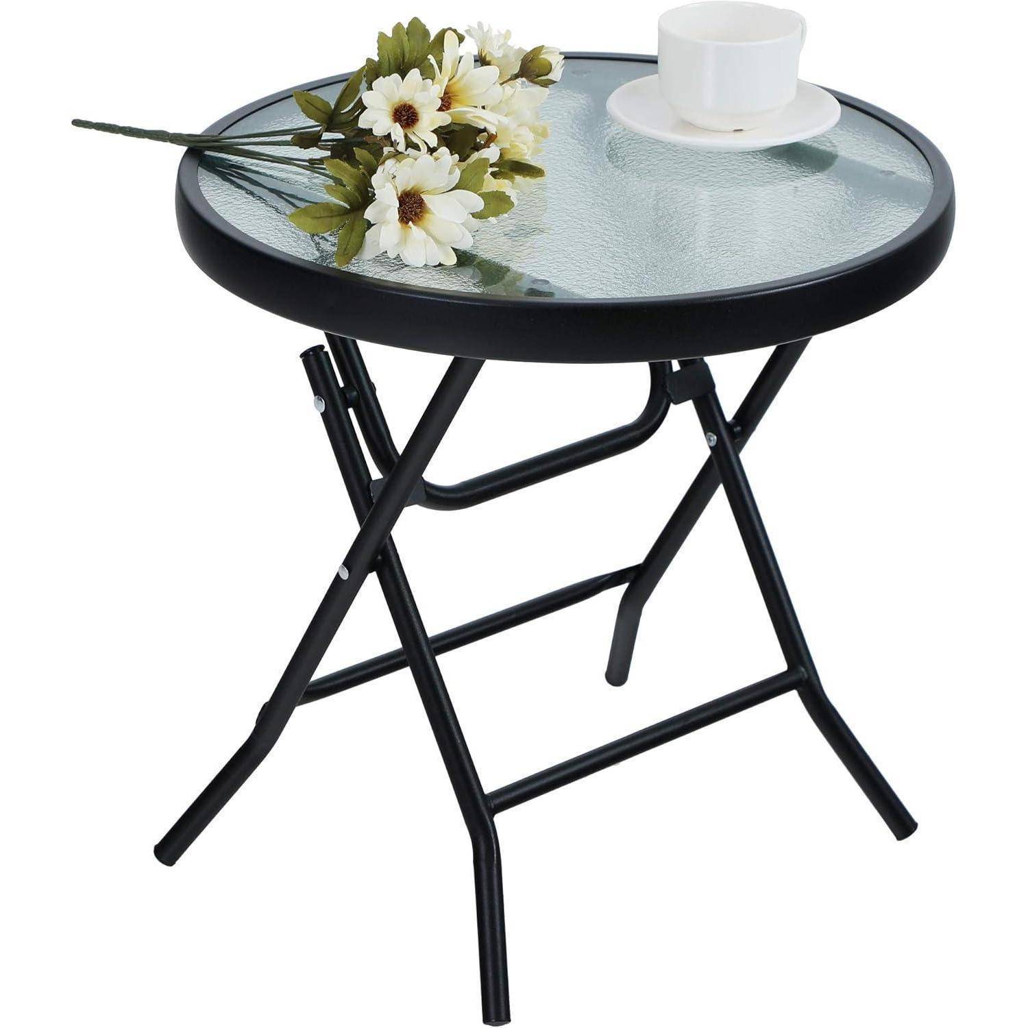 Ein kleiner runder Glastisch mit schwarzen Metallbeinen, auf dem eine weiße Tasse und Untertasse sowie ein Blumenstrauß weißer Gänseblümchen stehen.