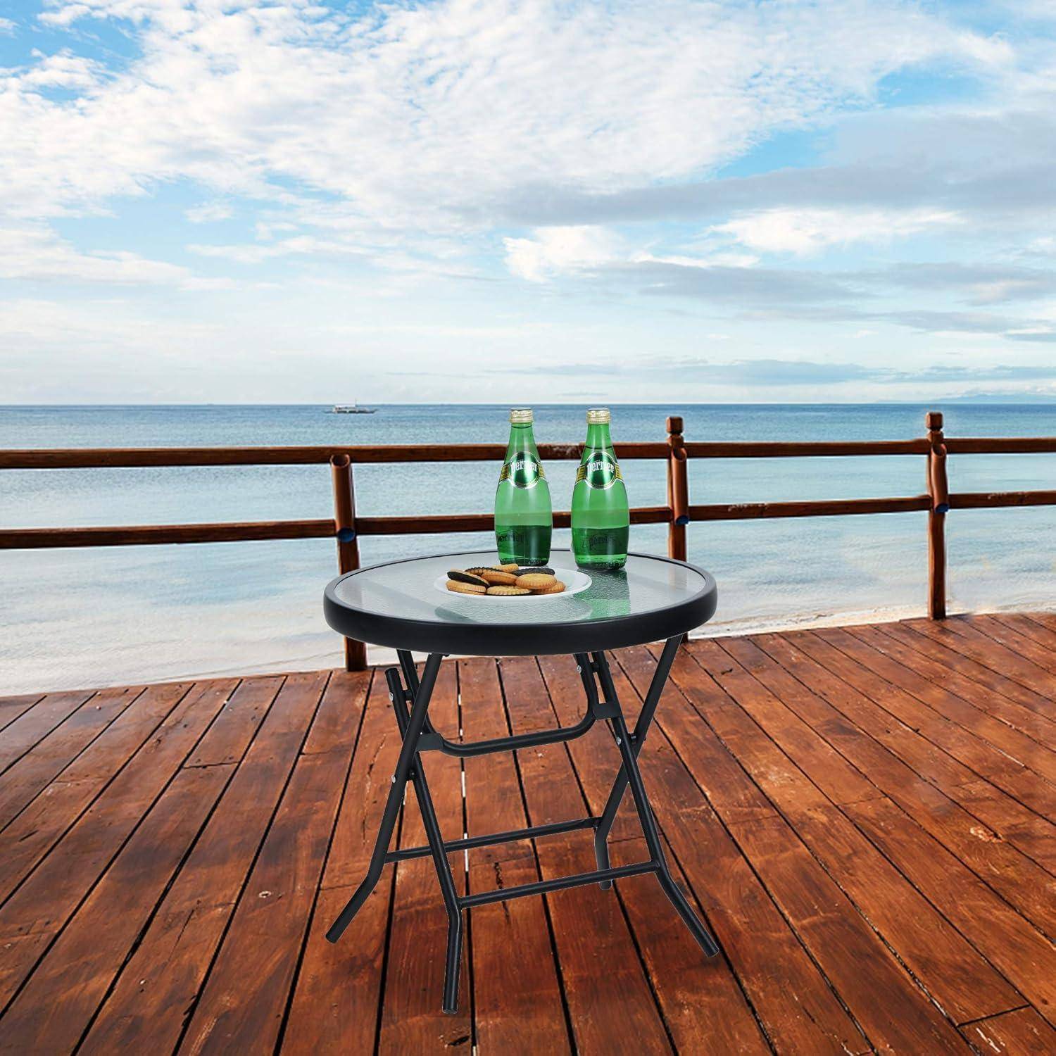 Ein runder Tisch auf einer Holzterrasse mit Blick aufs Meer, zwei grüne Flaschen und einem kleinen Teller. Der Himmel ist teilweise bewölkt.