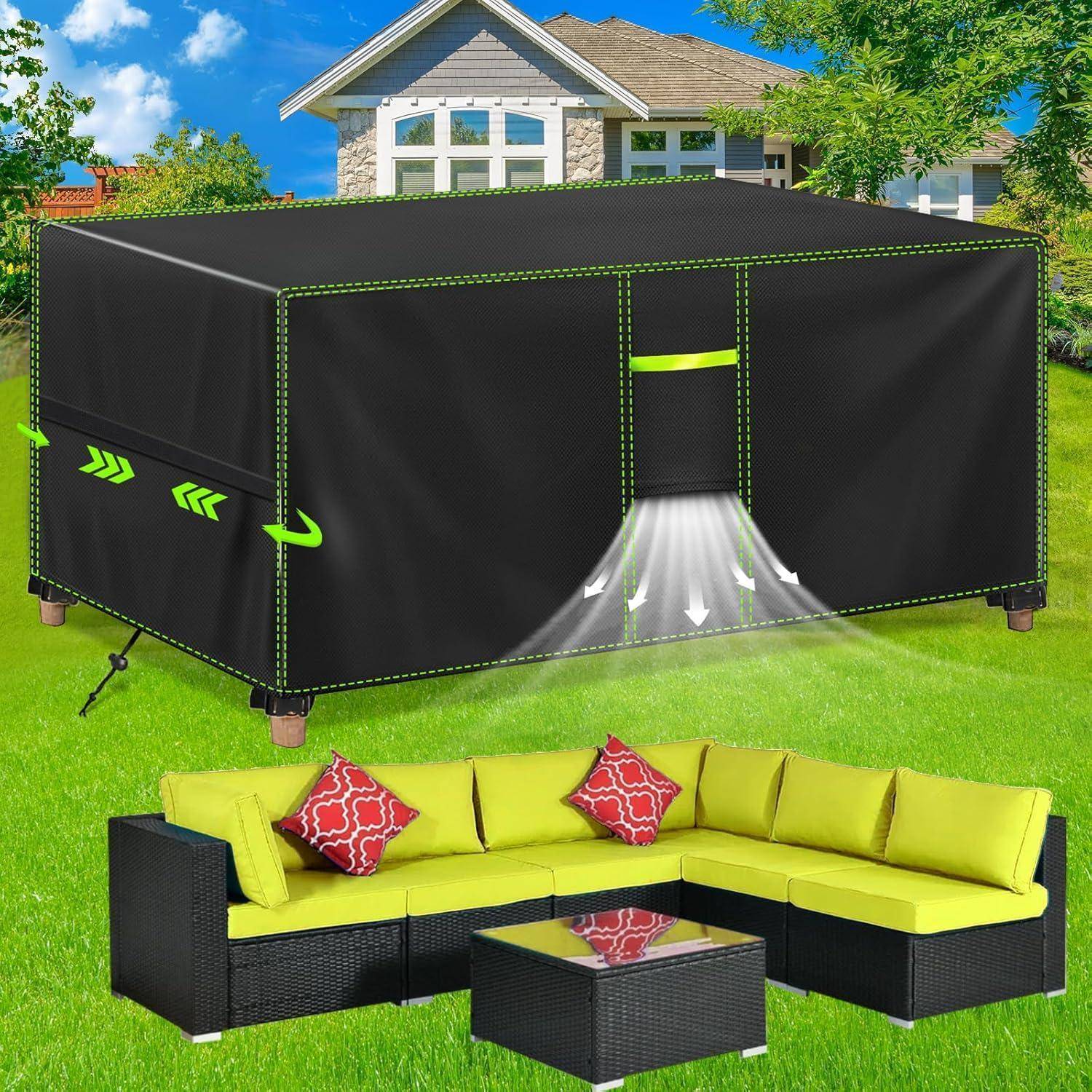 Eine Gartengarnitur mit grünen Kissen und einer passenden schwarzen Abdeckung auf dem Tisch, auf Gras stehend mit einem Haus im Hintergrund.
