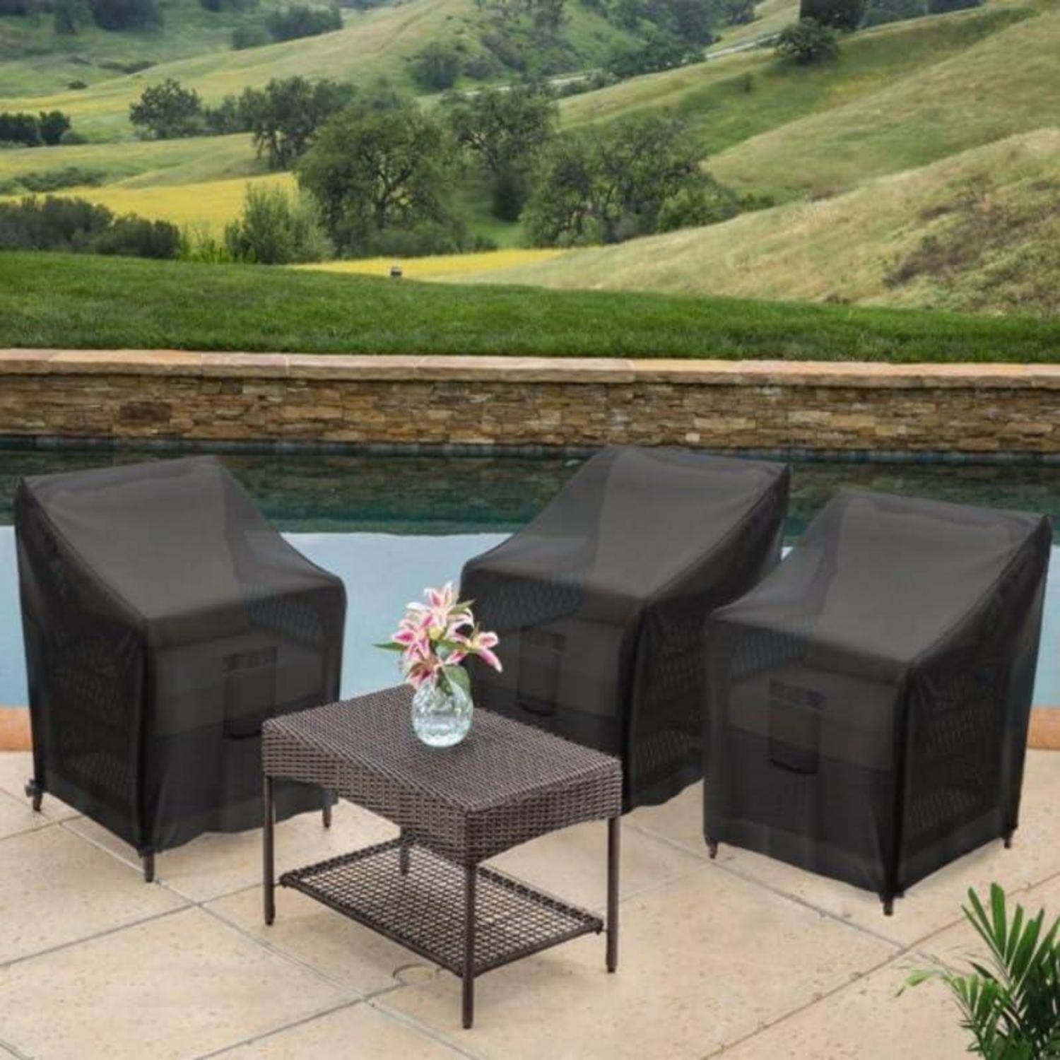 Drei Korbstühle und ein Tisch mit Blumen stehen auf einer Terrasse neben einem Pool und bieten einen Blick auf eine üppige grüne Landschaft mit Hügeln.