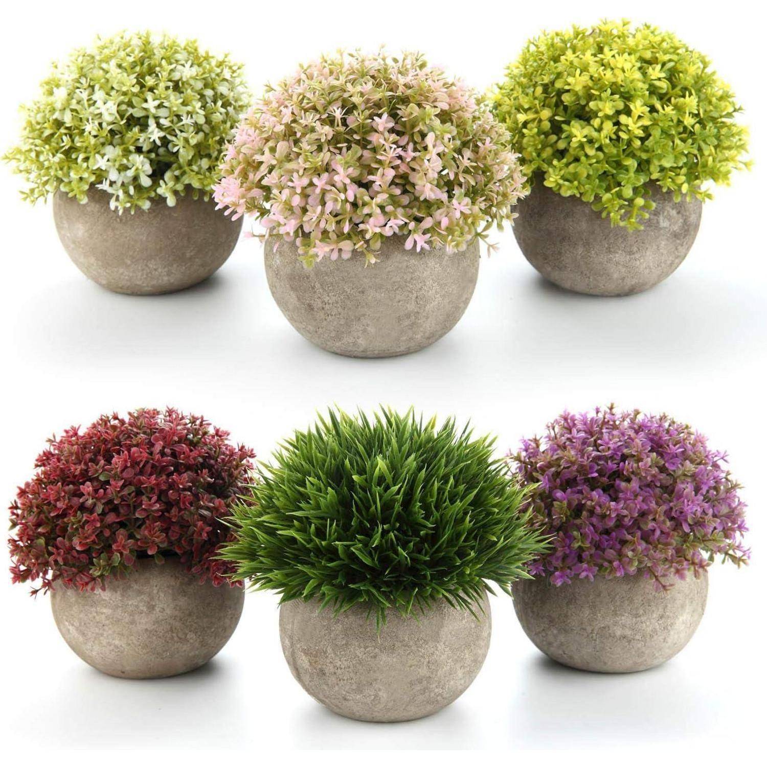Sechs runde Töpfe mit kleinen künstlichen Pflanzen in verschiedenen Farben: grün, pink, gelb, rot, grasgrün und lila.