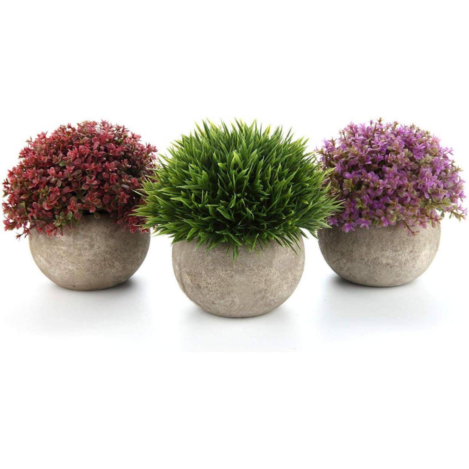 Drei runde Töpfe mit künstlichen Pflanzen: einer mit roten Blumen, einer mit grünem, grasartigem Blattwerk und einer mit lila Blumen.