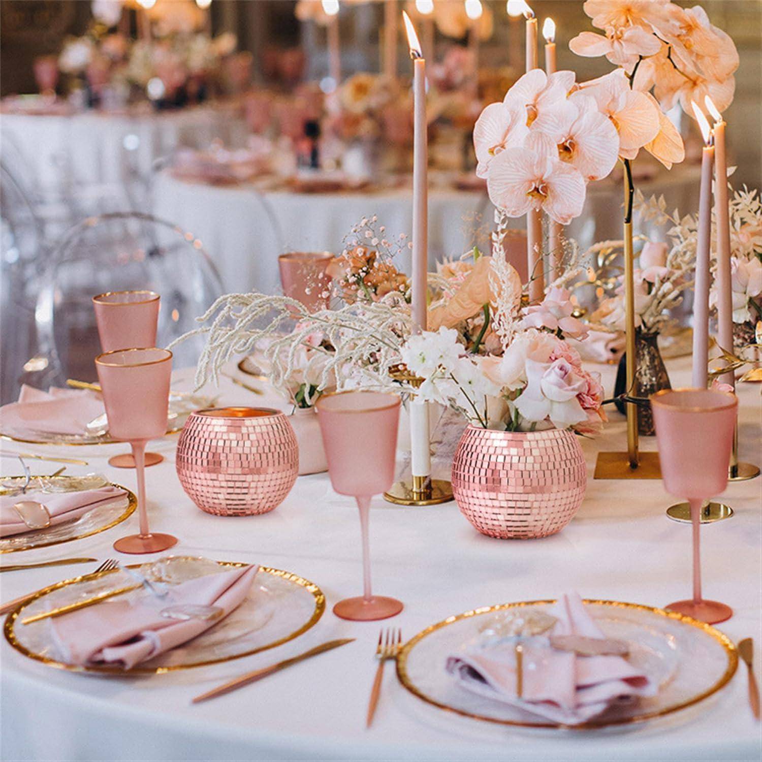 Elegante Tischgedeck mit rosa und goldenen Akzenten, mit hohen Kerzen, Blumenmittelstück mit Orchideen und dekorativem Glasgeschirr.