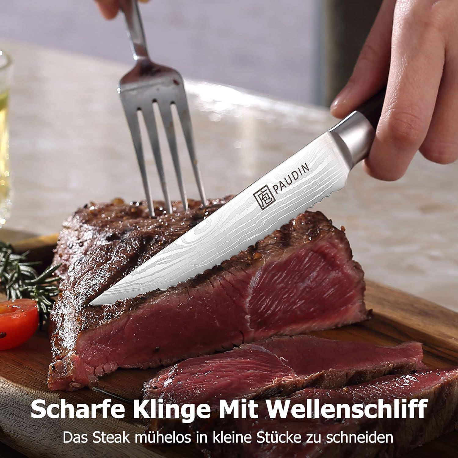 Ein Messer mit der Marke 'Paudin' schneidet ein gekochtes Steak auf einem Holzbrett, begleitet von einer Gabel, mit Kräutern und einer Tomatenscheibe in der Nähe.