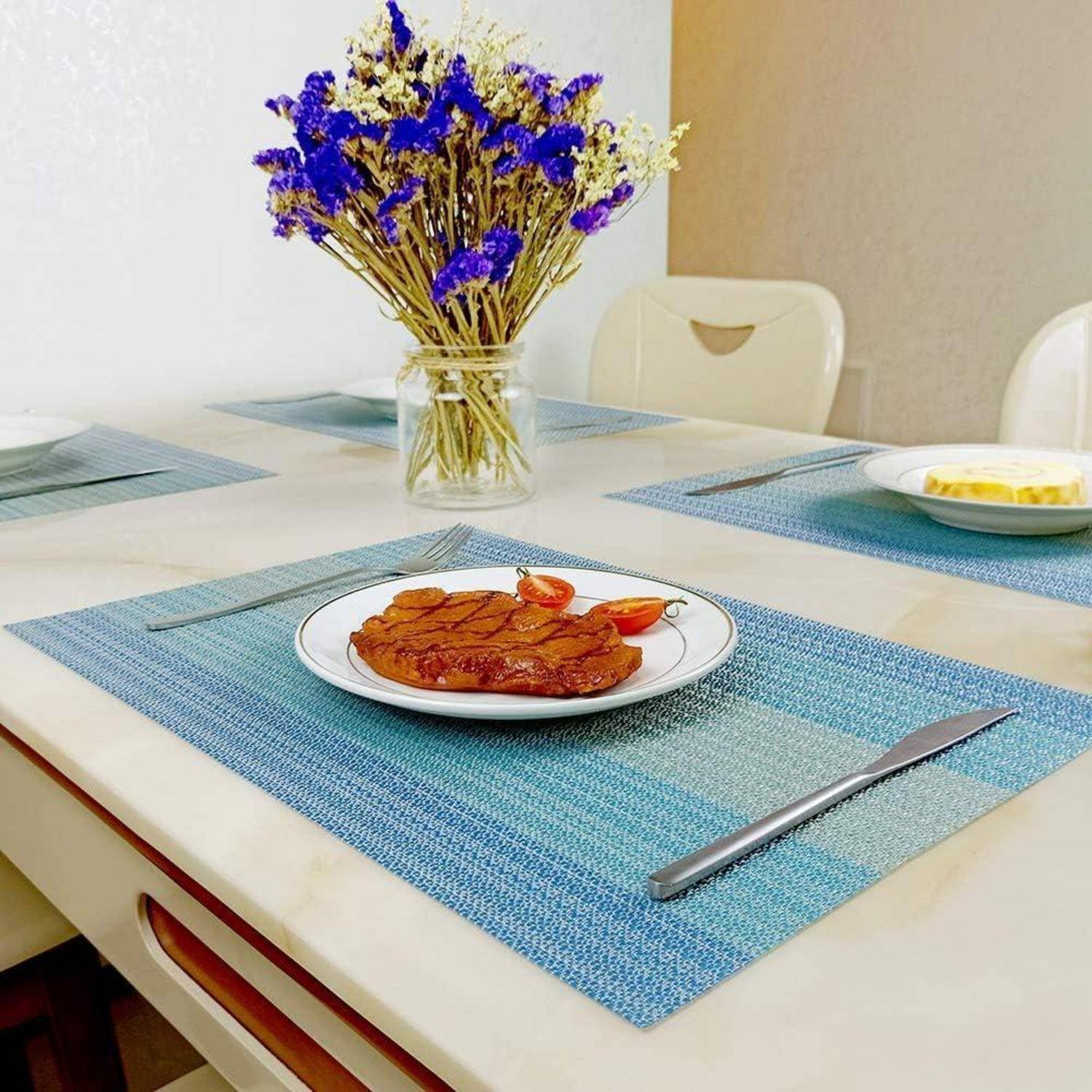 Ein Teller mit geschnittenen Pfirsichen auf einer Tischdecke mit einer blauen Tischdecke und einer Vase mit lila und gelben Blumen im Hintergrund.
