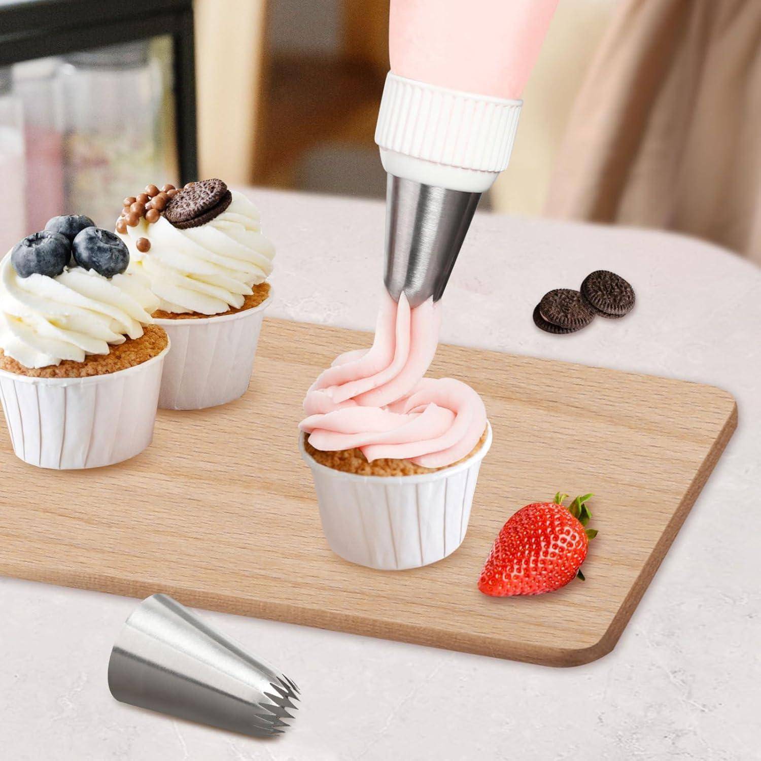 Eine Person dekoriert Cupcakes mit rosa Frosting mit einem Spritzbeutel. Zwei Cupcakes haben Schlagsahne und Beeren. Eine Erdbeere und Kekse liegen daneben.