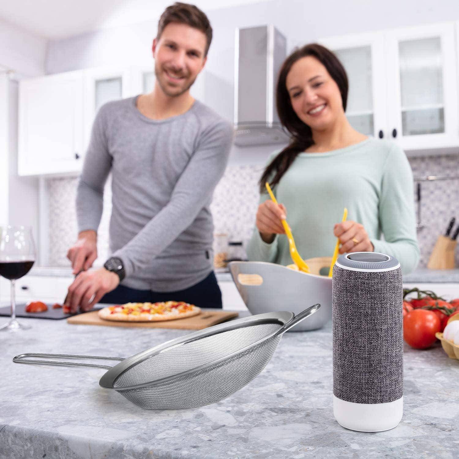 Ein Mann und eine Frau kochen gemeinsam in einer modernen Küche und lächeln. Ein Sieb und ein intelligenter Lautsprecher stehen auf der Arbeitsplatte.