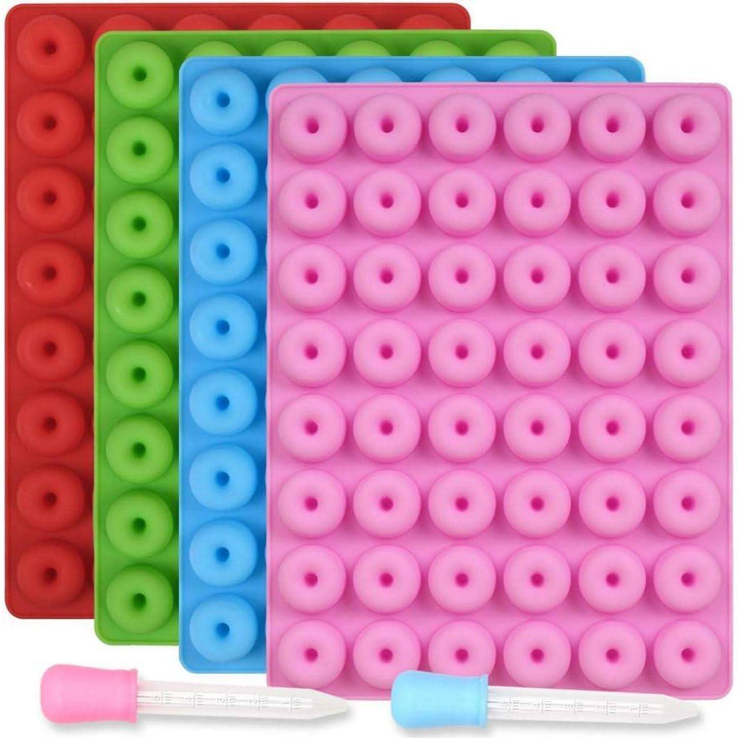 Vier Silikonform-Tabletts in Rot, Grün, Blau und Rosa, jedes mit runden Vertiefungen. Zwei Pipetten befinden sich vor den Tabletts.