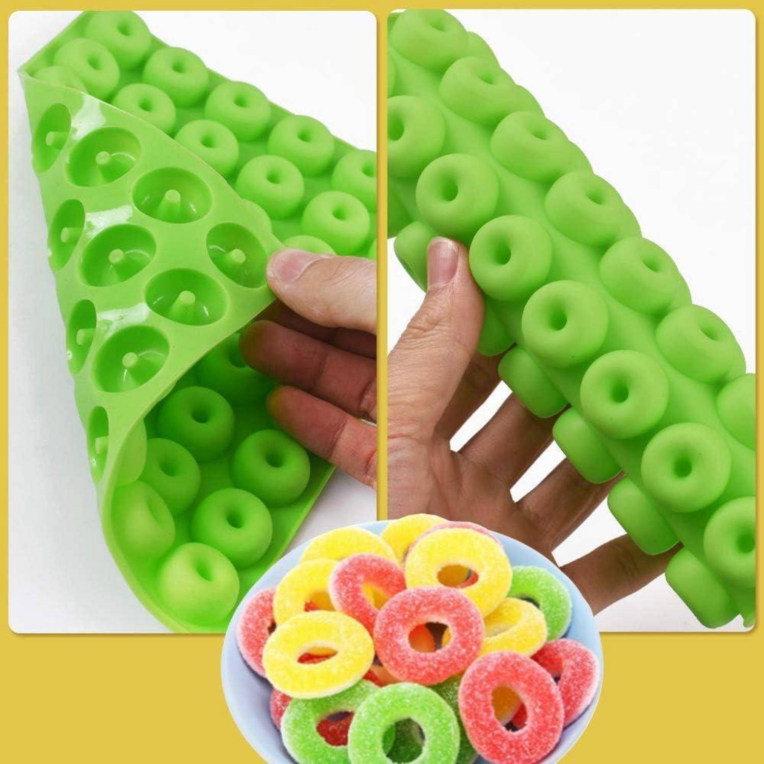 Eine grüne Silikonform zum Herstellen von Gummiring wird gezeigt, wobei eine Hand die Flexibilität demonstriert. Eine Schüssel mit bunten Gummiringen befindet sich darunter.