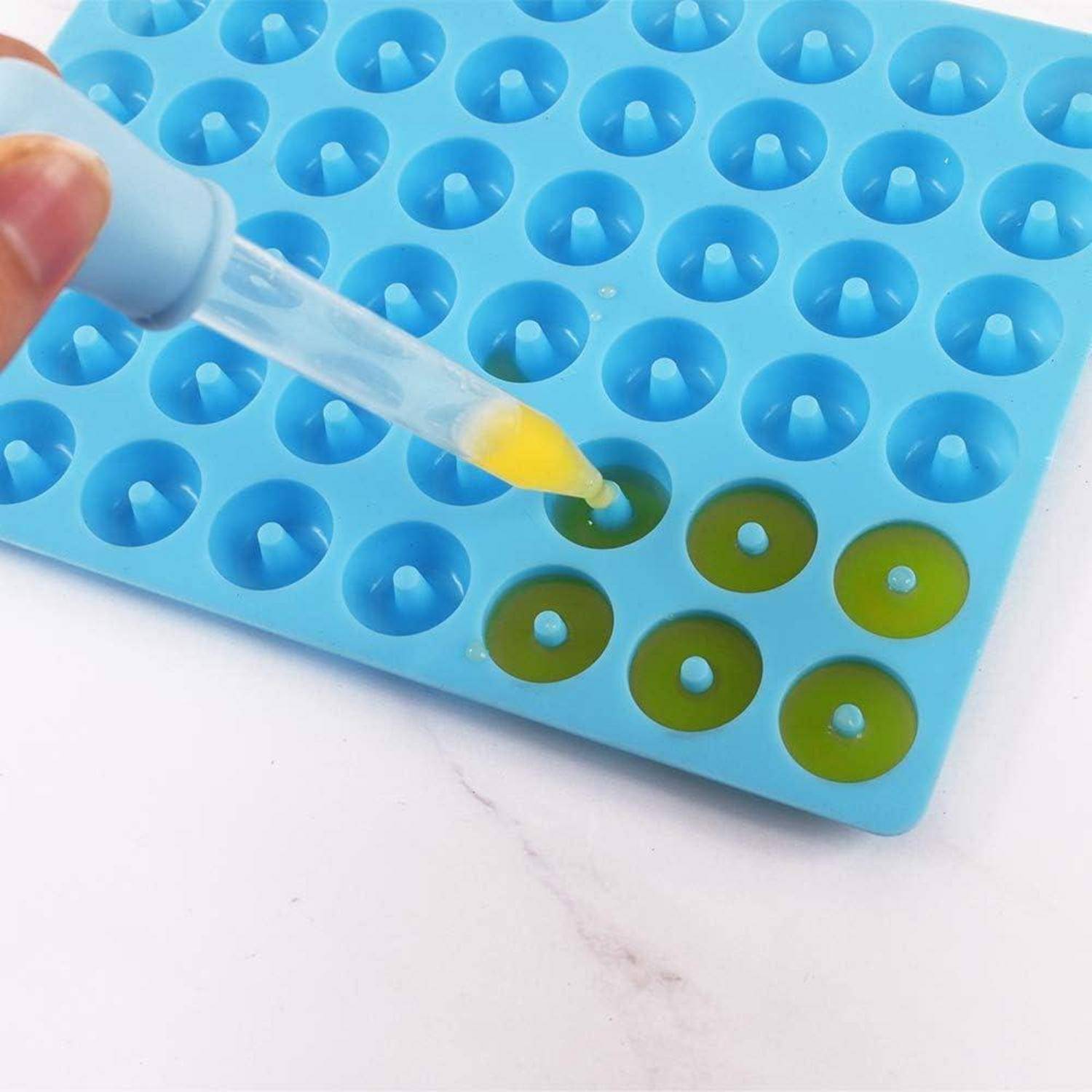 Eine Pipette gibt gelbe Flüssigkeit in eine blaue Silikonform, die grüne Flüssigkeit enthält, höchstwahrscheinlich für ein wissenschaftliches Experiment oder eine Bastelaktivität.