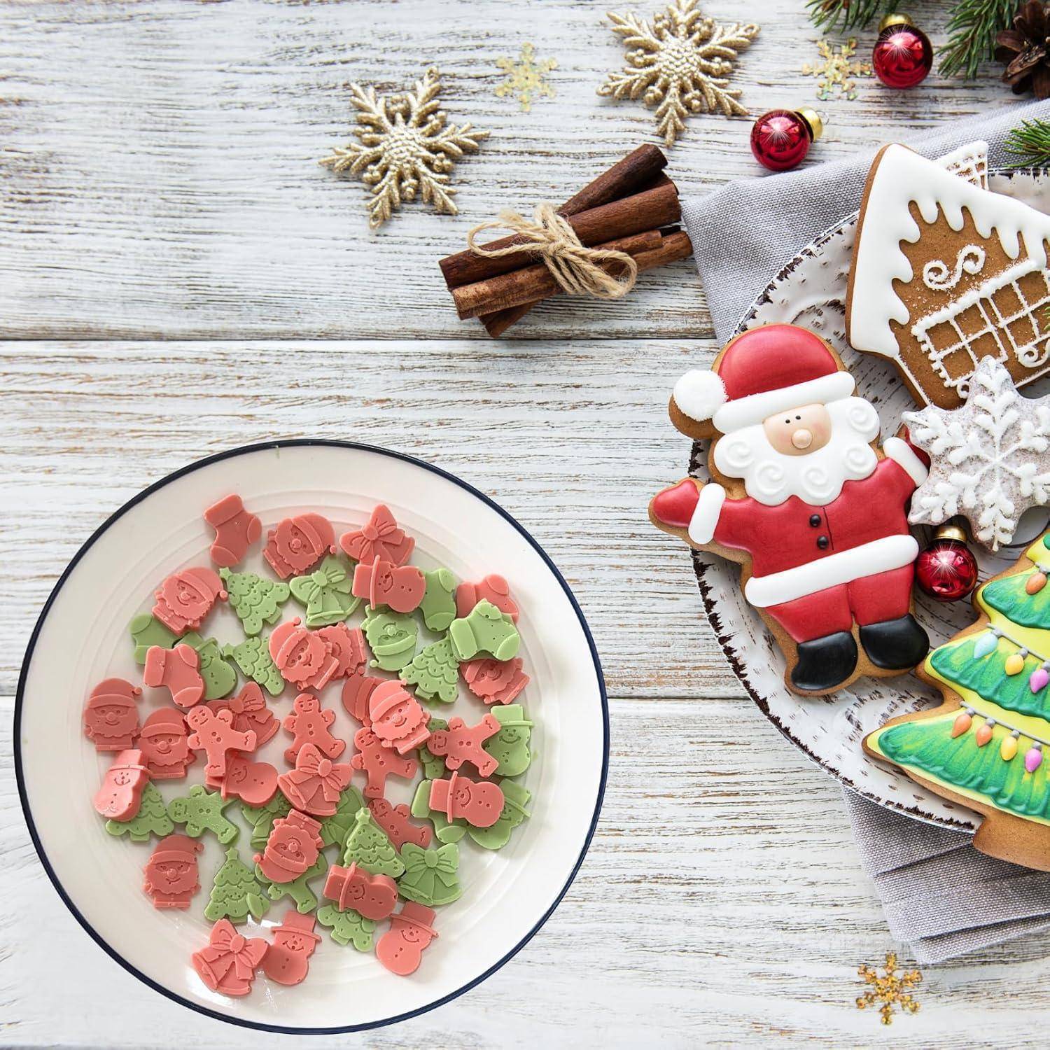 Festliche Plätzchen auf einem Tisch, geformt wie der Weihnachtsmann, ein Weihnachtsbaum und ein Lebkuchenhaus, daneben ein Teller mit dekorativen Keksen.