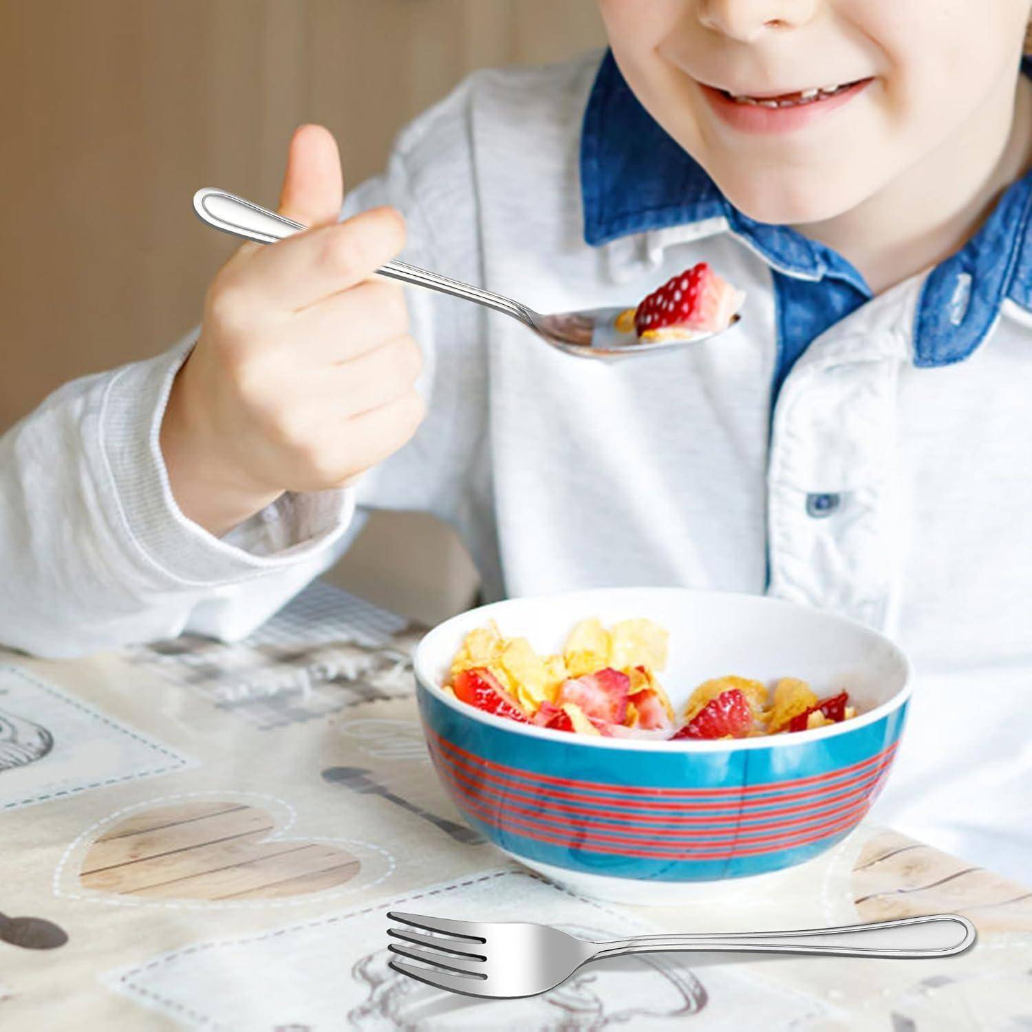 Ein Kind in einem blauen Hemdkragen lächelt, während es Joghurt mit Erdbeeren und Bananenscheiben aus einer bunten Schüssel auf einem Tisch isst.