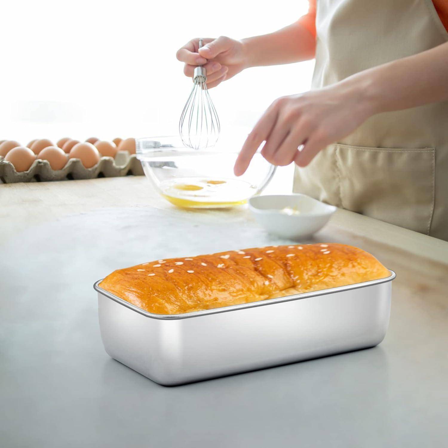 Eine Person schlägt Eier in einer Glasschüssel auf einer Arbeitsplatte, neben einer Brotform mit Brot und einem Eierkarton in der Nähe.