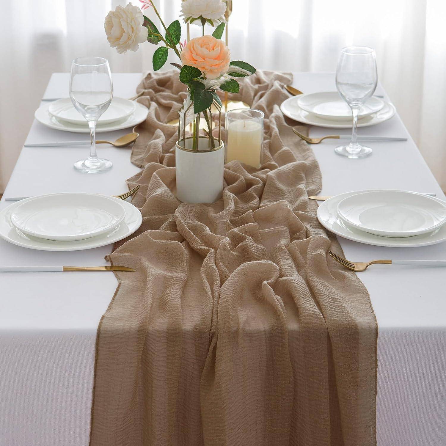 Elegante Tischdecke mit einem beigen Tischläufer, weißen Tellern, Weingläsern, Kerzen und einer Vase mit Rosen.