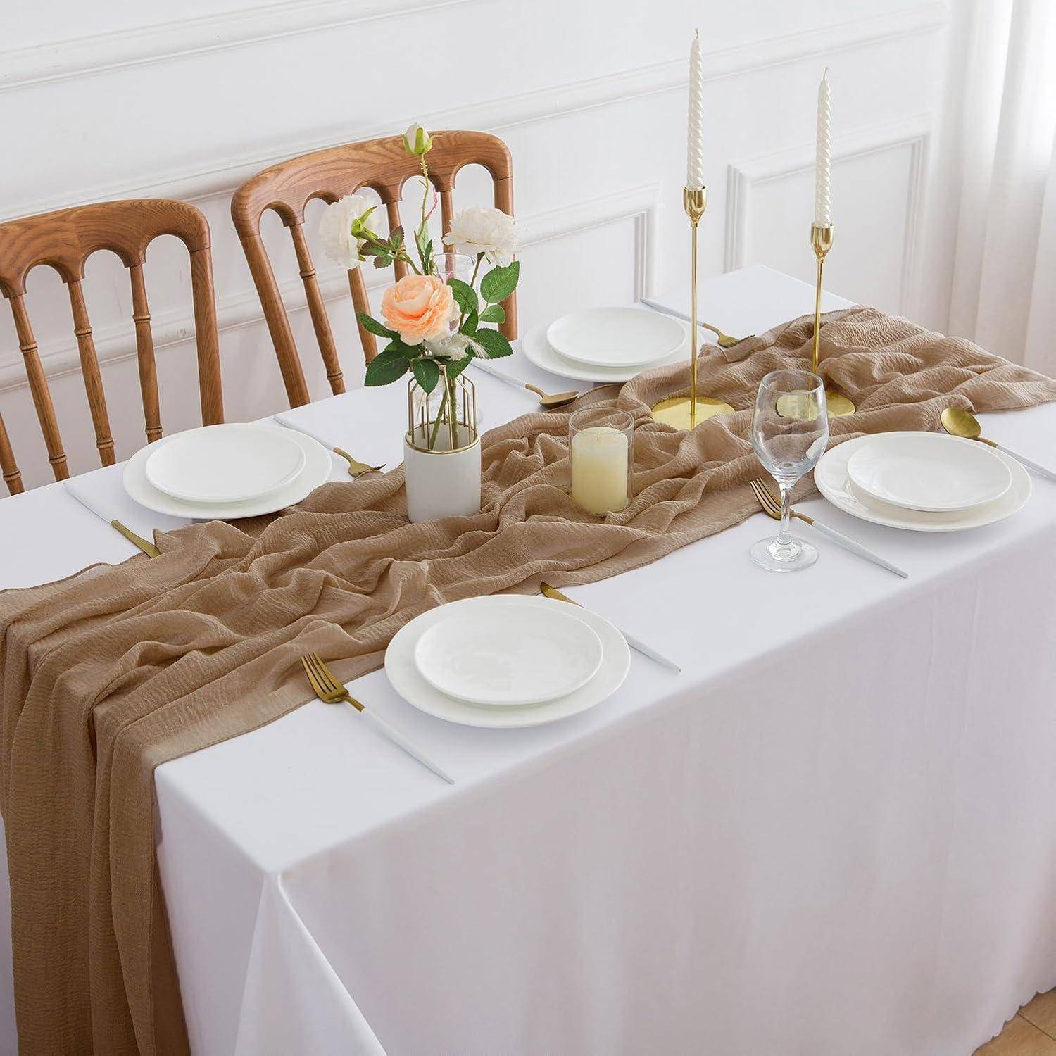 Elegante Tischdecke mit weißem Tischdecken, neutralem Läufer, weißen Tellern, Weingläsern, Kerzen und einem floralen Mittelstück in einer Vase.