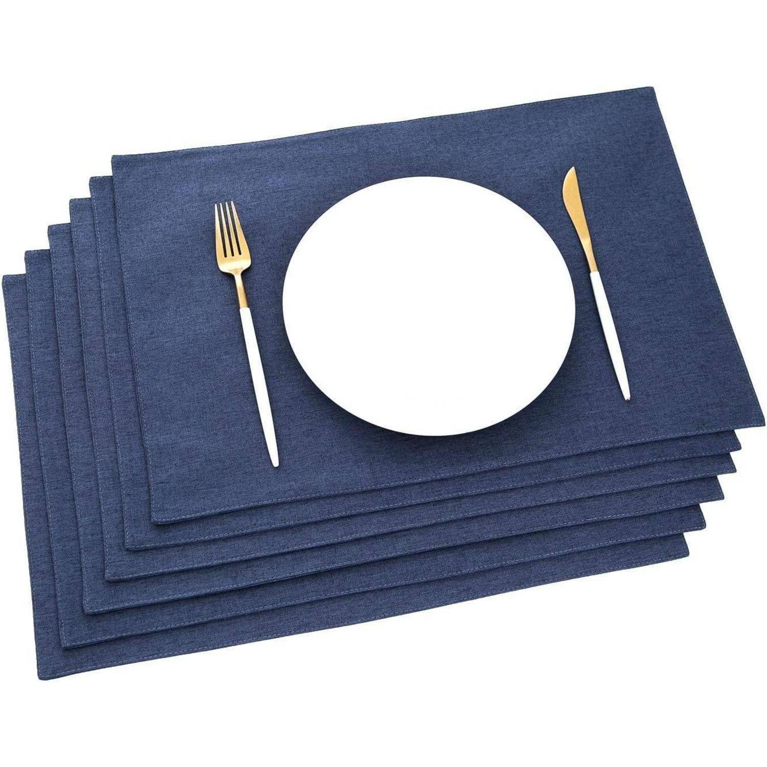 Ein Stapel marineblauer Platzdeckchen mit einem goldenen Messer und einer Gabel, die links und rechts von einem weißen Teller auf dem obersten Platzdeckchen platziert sind.