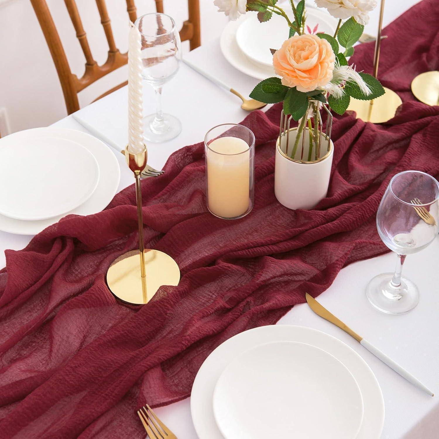Ein für ein formelles Ereignis gedeckter Tisch mit weißen Tellern, goldenen Bestecken, Weingläsern und einem burgunderroten Tischläufer. Blumen und Kerzen als Tischdekoration.