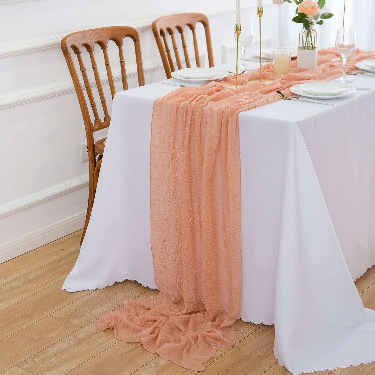 Tisch mit elegantem pfirsichfarbenem Stoffläufer, drei Holzstühlen, Kerzen und einer einzelnen Rose in einer Vase, die eine romantische Atmosphäre schafft.
