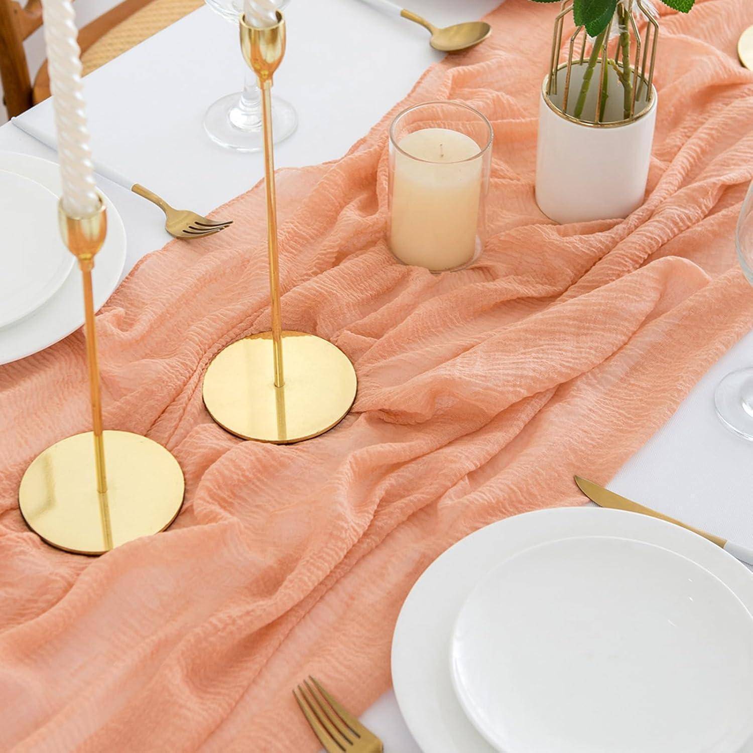 Ein Esstisch, der mit einem pfirsichfarbenen Tischdecken, weißen Tellern, goldenen Bestecken und goldenen Kerzenhaltern gedeckt ist, schafft eine elegante Atmosphäre.