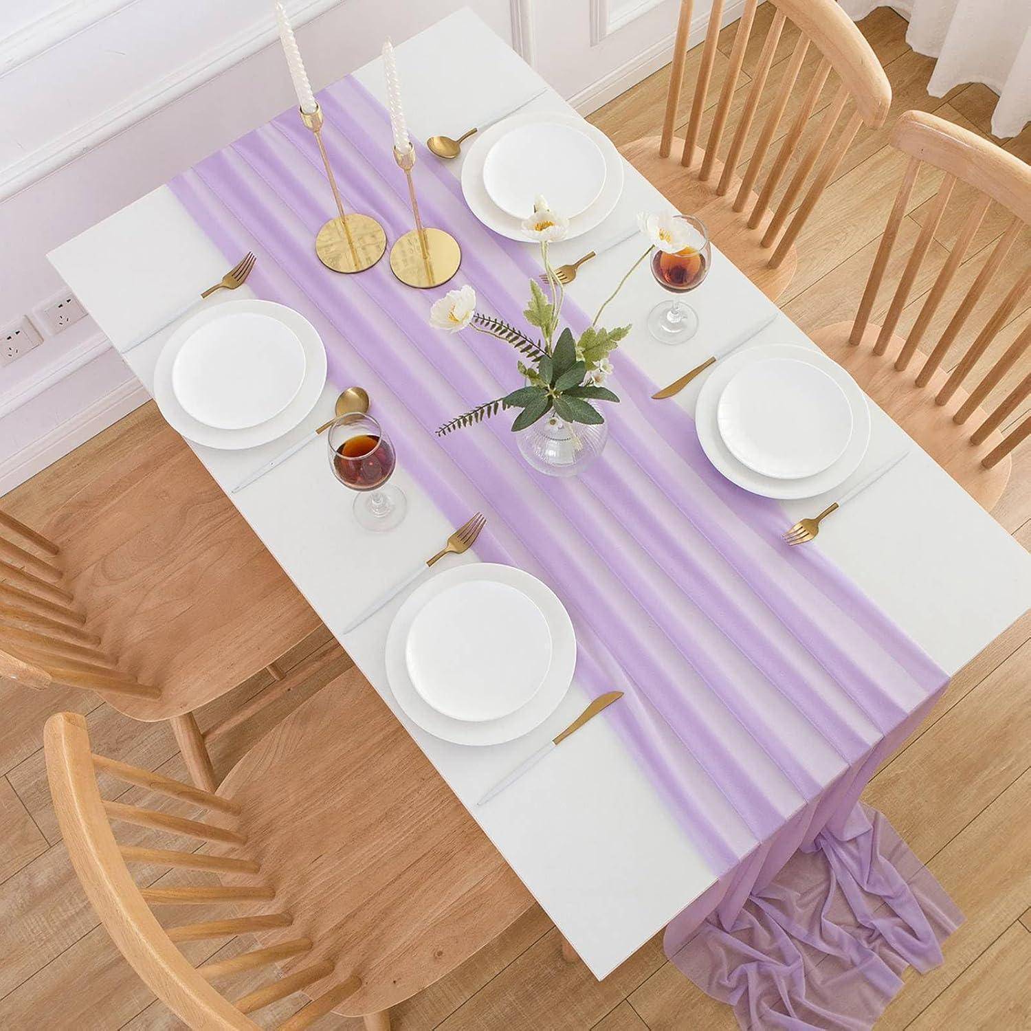 Ein rechteckiger Esstisch, gedeckt für sechs Personen, mit weißen Tellern, goldenem Besteck und Gläsern. Ein Lavendel-Tischläufer und ein Mittelstück verleihen Eleganz.