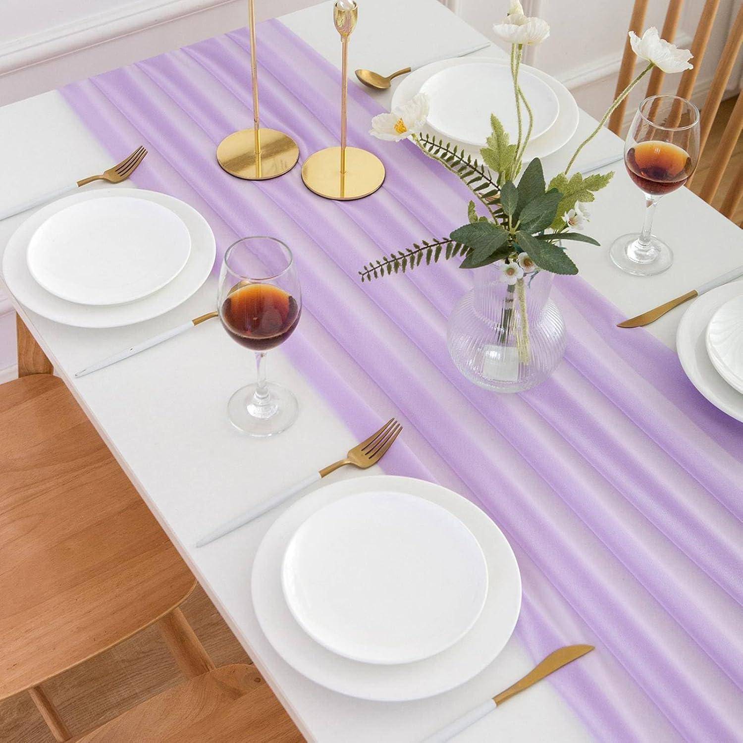 Ein Esstisch, gedeckt mit weißen Tellern, goldenen Bestecken, einem violett gestreiften Tischläufer, Rotwein in Gläsern und einer Vase mit Blumen.