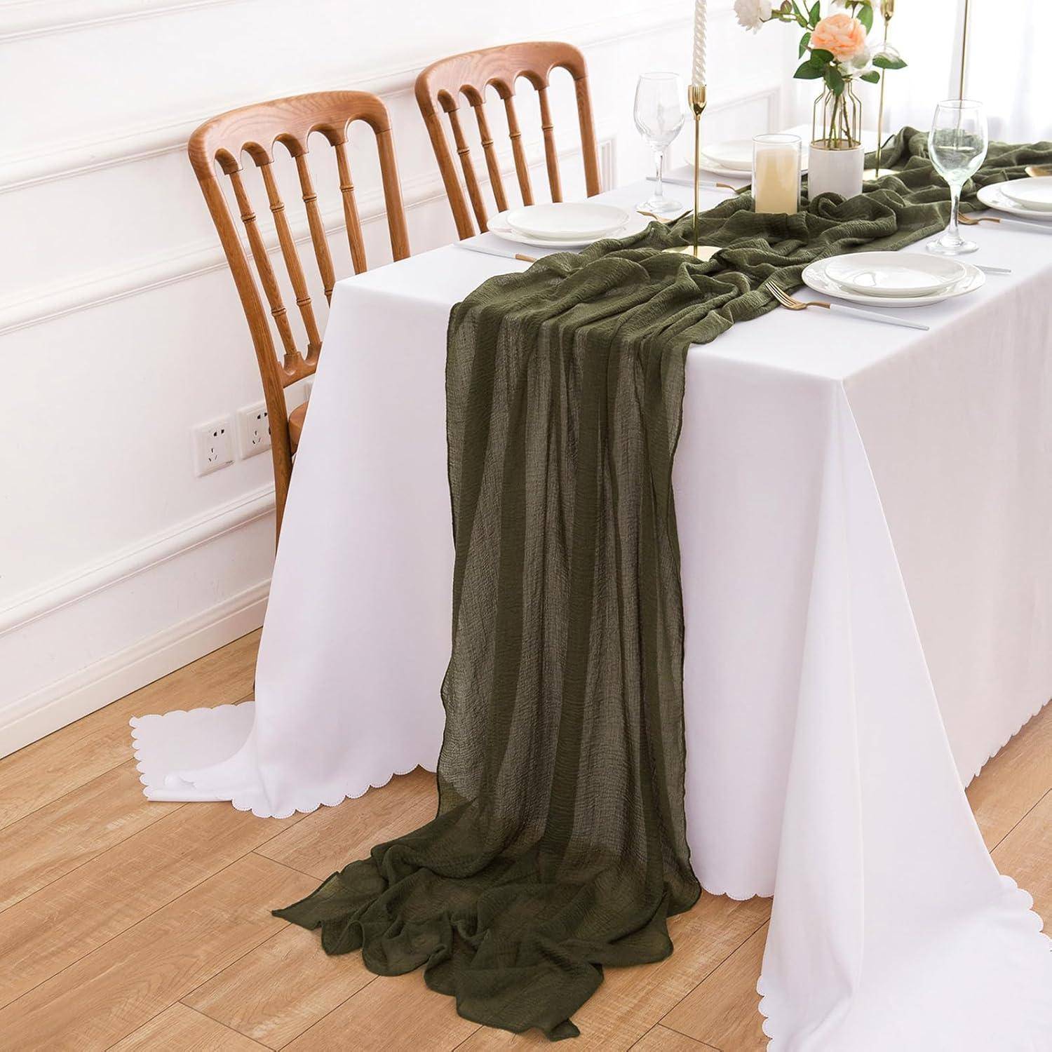 Ein Esstisch für vier Personen, dekoriert mit einem dunkelgrünen Tischläufer, weißer Tischdecke und eleganter Blumenmitteldecke, vorbereitet für eine formelle Mahlzeit.
