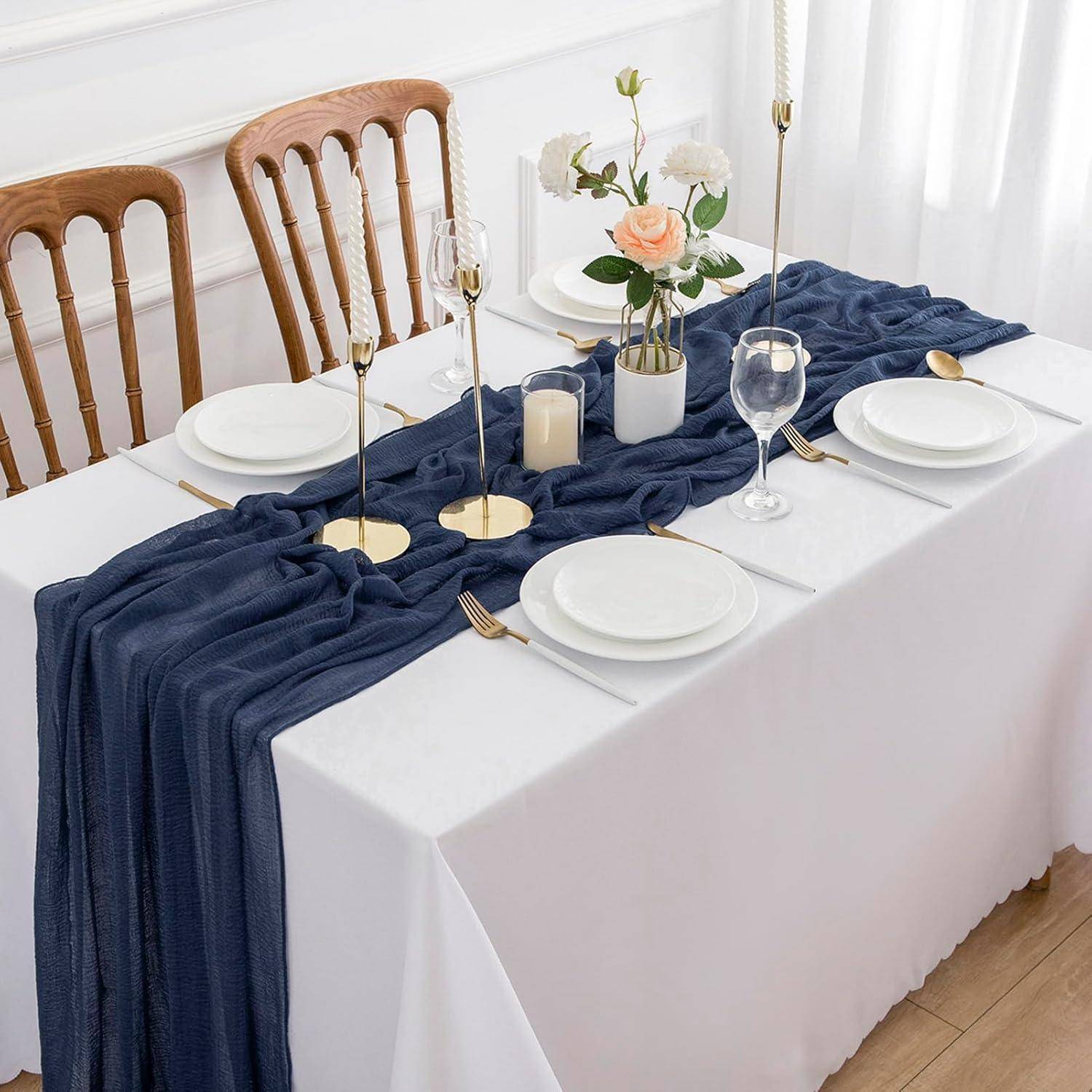 Ein formell gedeckter Esstisch für vier Personen, mit einem marineblau-farbenen Tischläufer, eleganten Tellern, goldenen Bestecken, Weingläsern und einem Blumenarrangement als Tischdekoration.