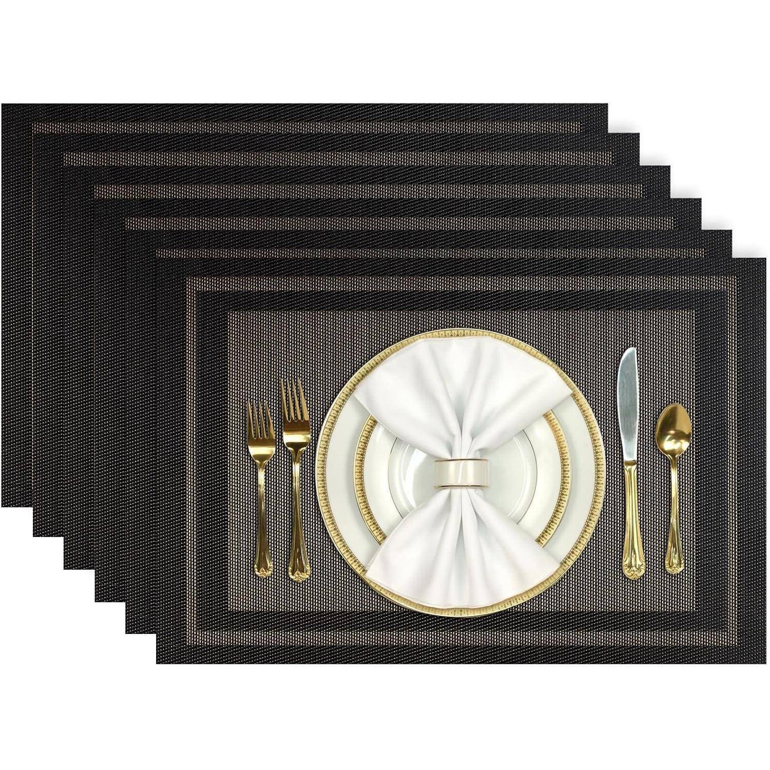 Ein formelles Gedeck mit einem schwarzen Platzdeckchen, goldenen Bestecken und einer weißen Serviette, die wie eine Schleife auf einem weiß-goldenen Teller angeordnet ist.