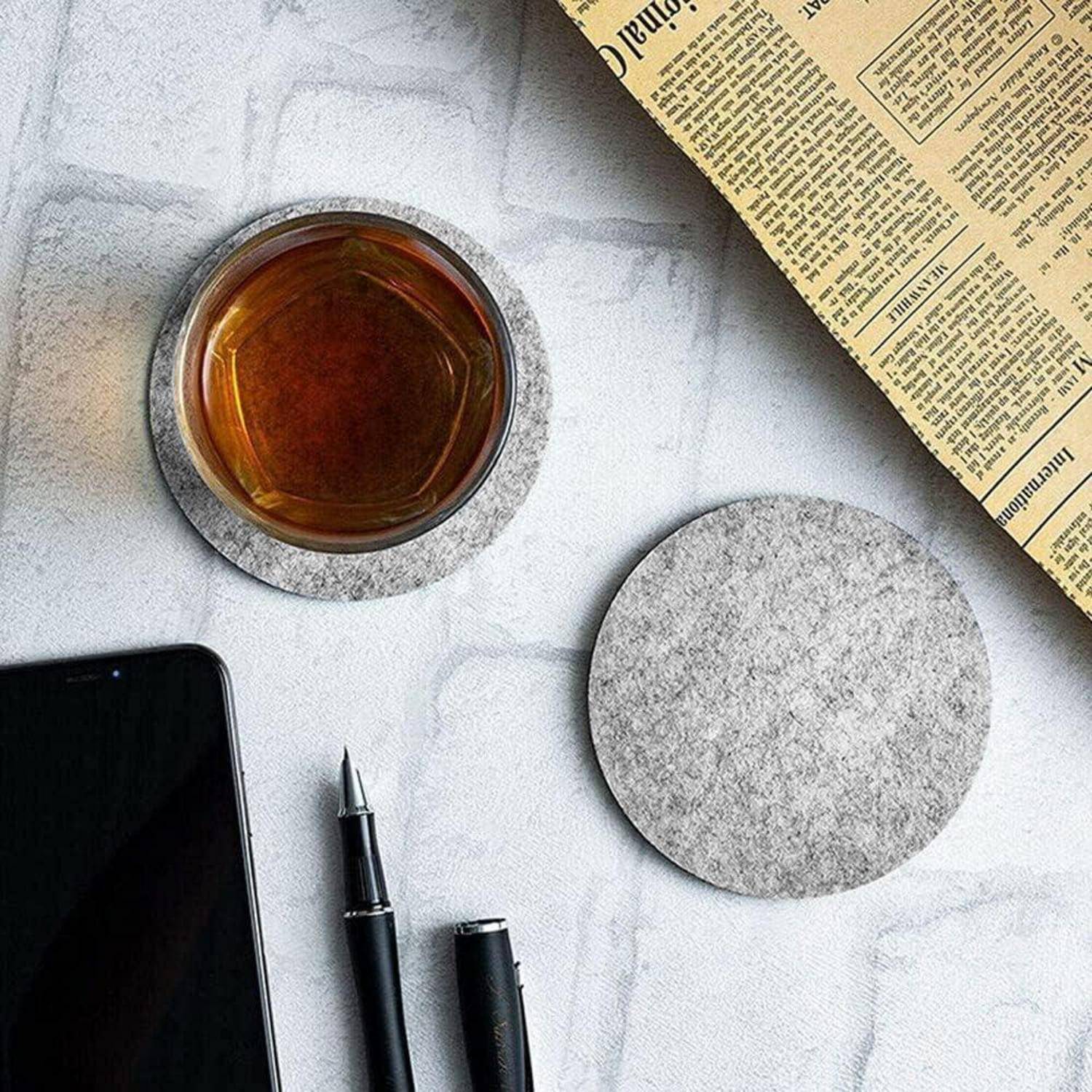 Eine Teetasse auf einem Untersetzer, neben einer aufgeschlagenen Zeitung, einem Stift und einem Smartphone auf einer hellen Oberfläche, was eine Morgenroutine andeutet.