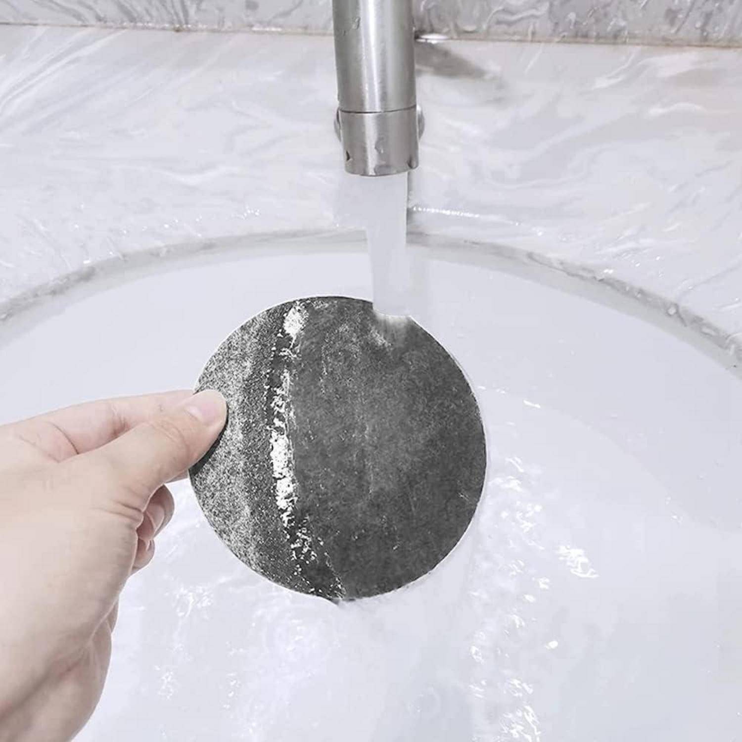 Eine Hand, die ein dunkles, rundes Objekt unter einem laufenden Wasserhahn hält. Das Wasser erzeugt eine reflektierende Oberfläche und betont die Textur des Objekts.