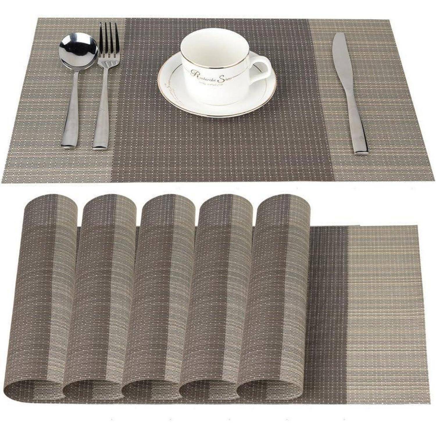 Ein Gedeck zeigt eine Gabel, einen Löffel und ein Messer auf einer geflochtenen Tischdecke mit einer weißen Tasse und Untertasse. Darunter liegen fünf aufgerollte Platzdeckchen.