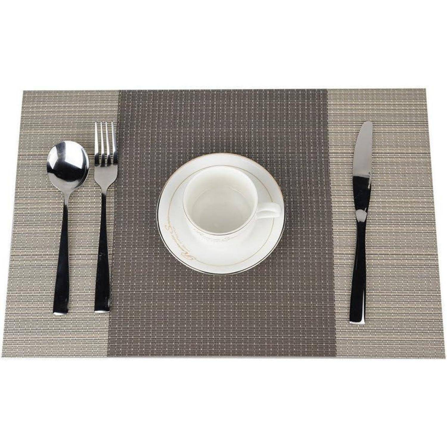 Ein Gedeck auf einem grauen Platzset mit einer Kaffeetasse und Untertasse in der Mitte, Gabel und Löffel links und Messer rechts.