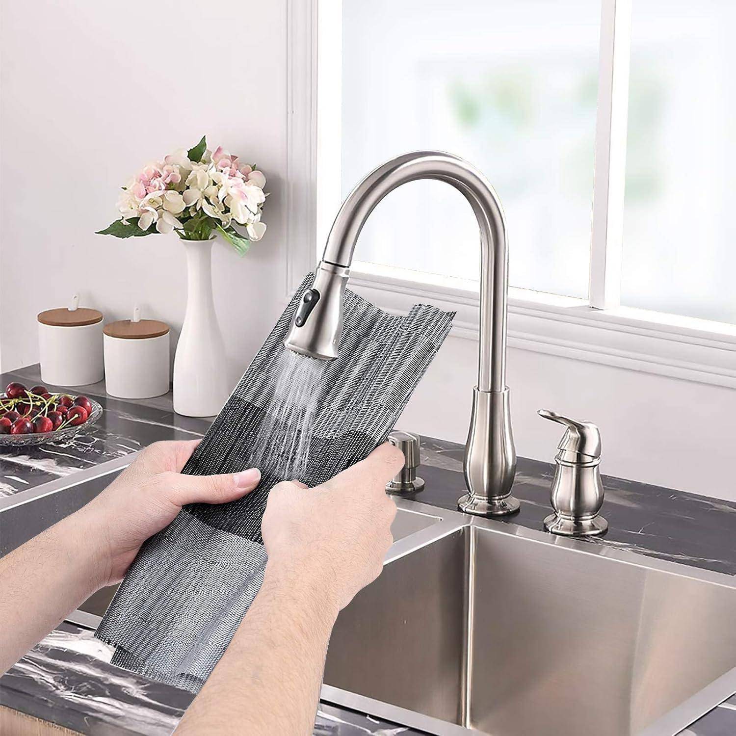 Eine Person spült ein rechteckiges Tablett unter einem modernen Wasserhahn in der Küche. Im Hintergrund befinden sich Blumen und Küchengegenstände auf der Arbeitsplatte.