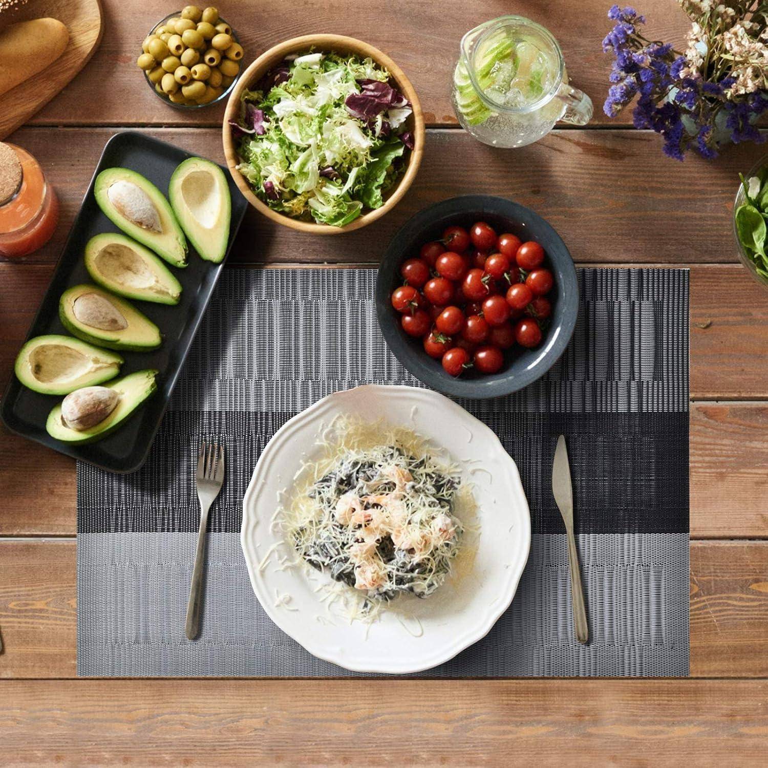 Gedeck mit Pasta-Gericht, Avocados, Salat, Kirschtomaten, Oliven und einem Getränk auf einem Holztisch, dekoriert mit lila Blumen.